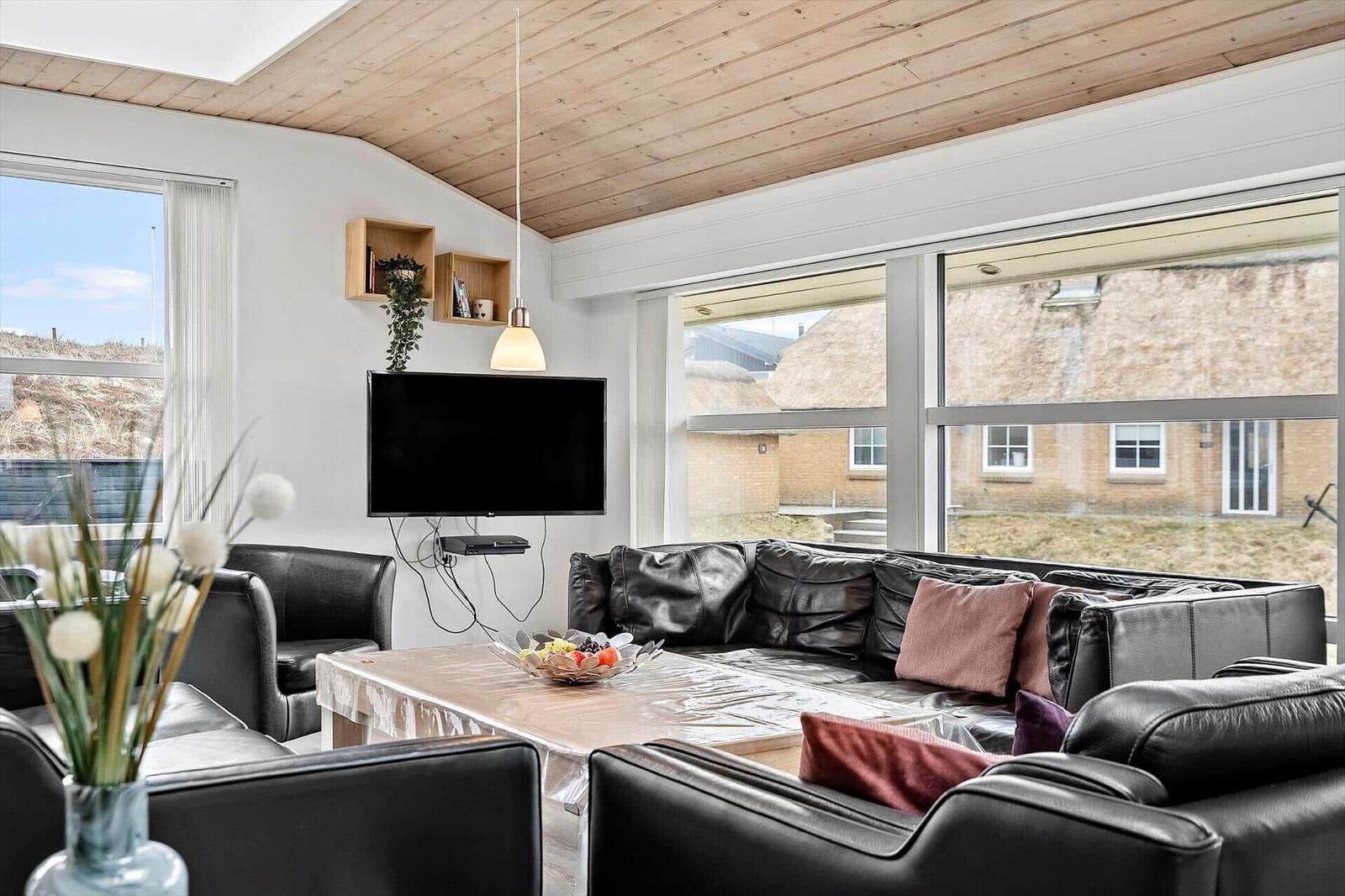 Wohnzimmer mit Ledersofa, Fernseher und großen Fenstern.