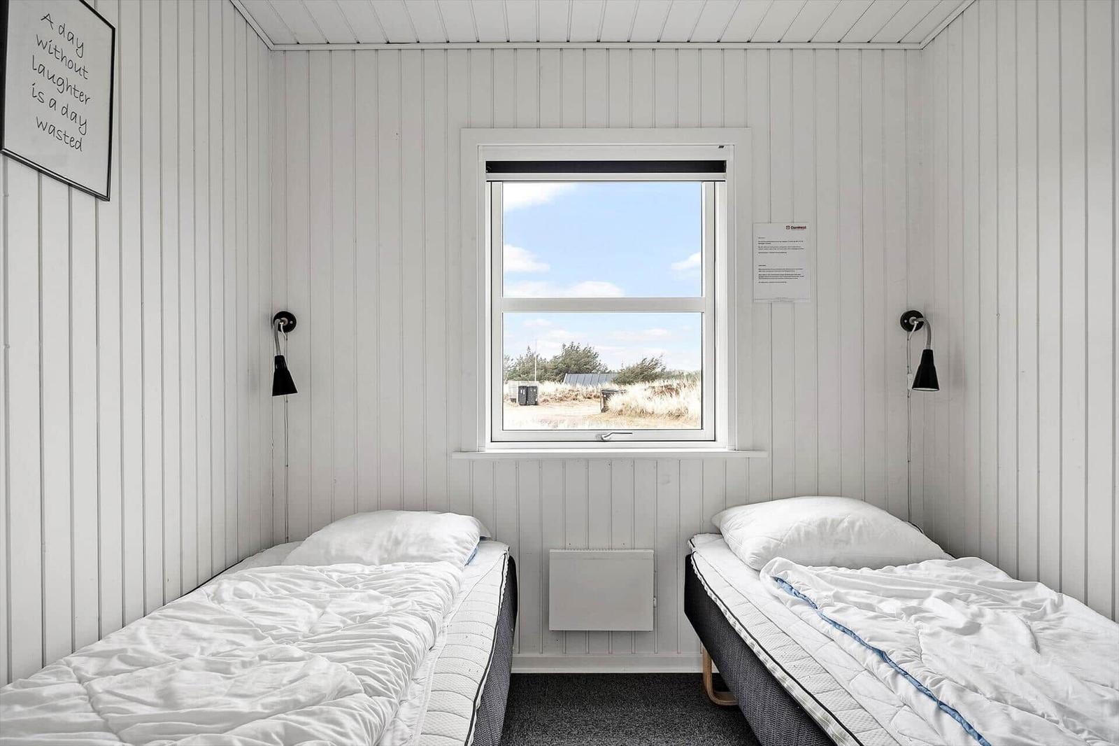 Zwei Betten mit weißen Bettwäschen, Fenster mit Blick auf Außengelände, weiße Holzwandverkleidung.