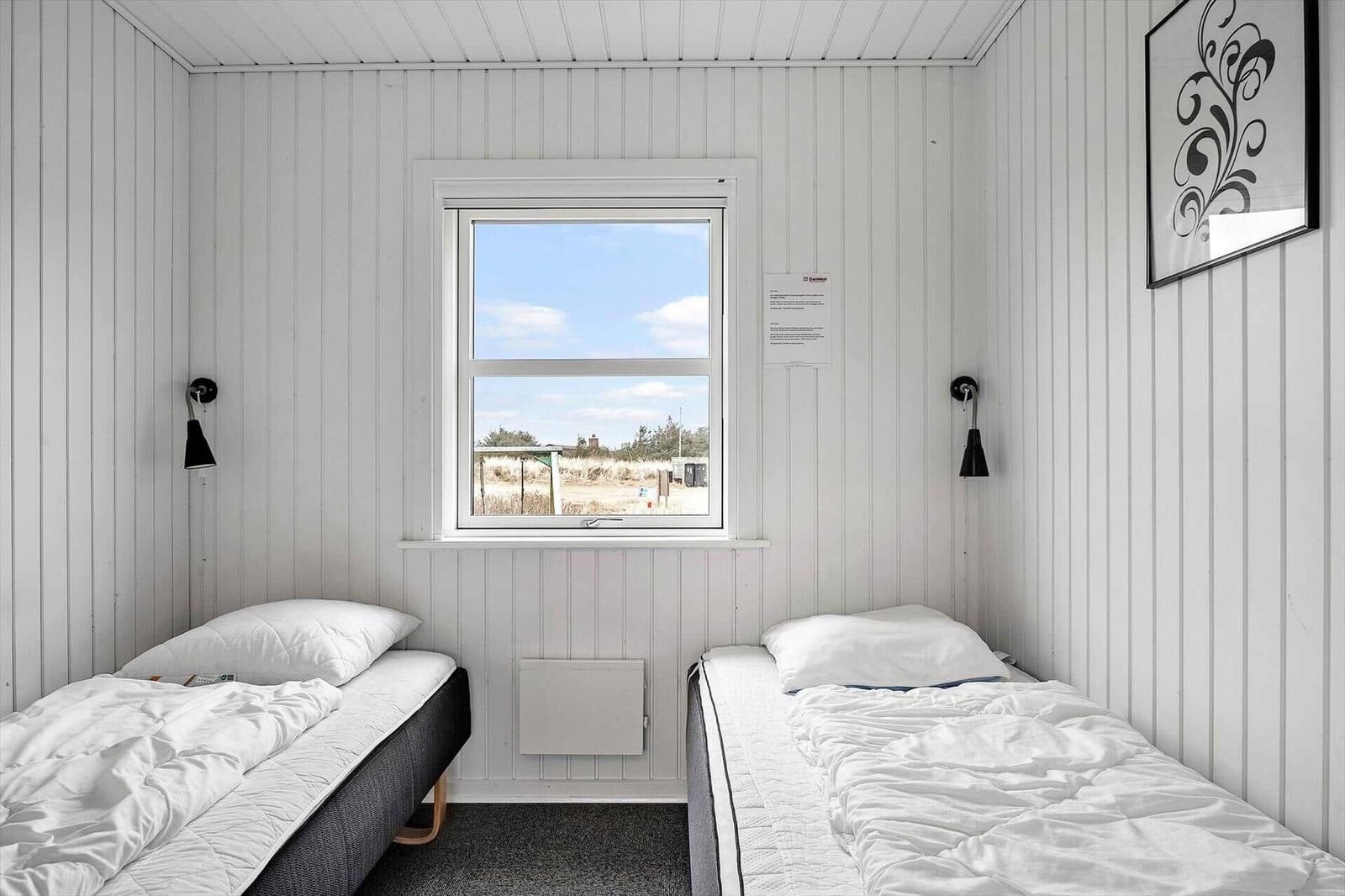 Zwei Einzelbetten mit weißen Bettwäsche, Fenster mit Blick nach draußen, weiße Holzwände.