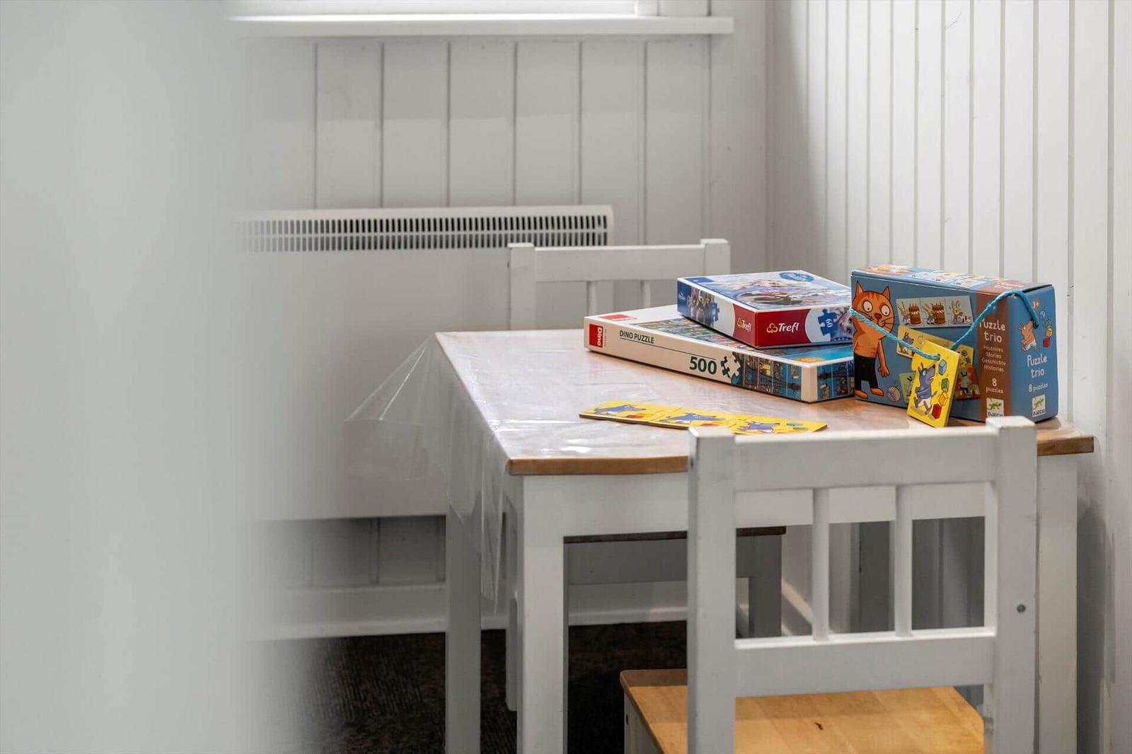 Tisch mit Stühlen und Kinderspielen in einem Raum mit weißer Wandverkleidung.