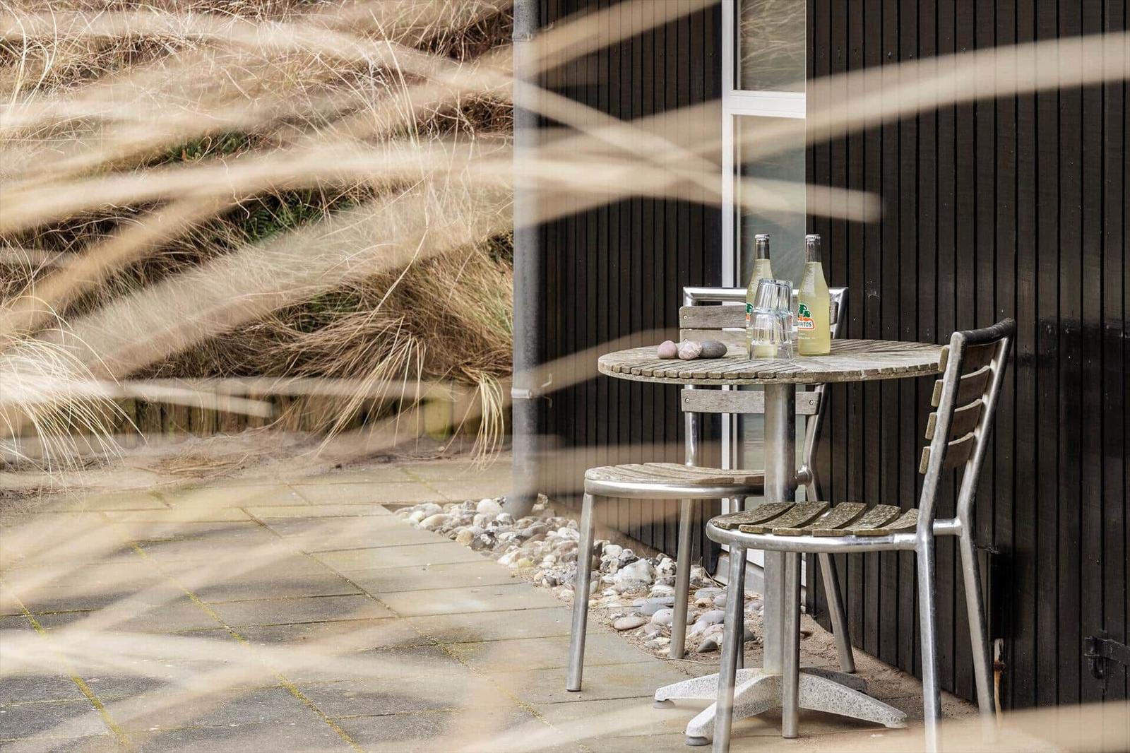 Außenbereich mit Tisch und Stühlen neben einer dunklen Holzwand.