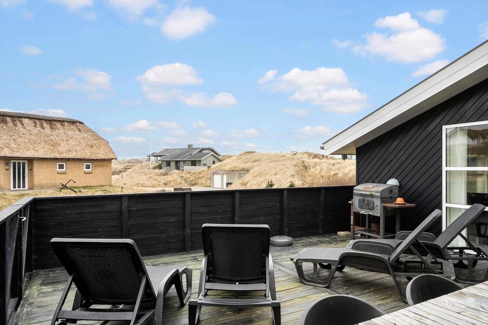 Terrasse mit Liegestühlen und Grill, Blick auf Dünenschutzwälle und Häuser.