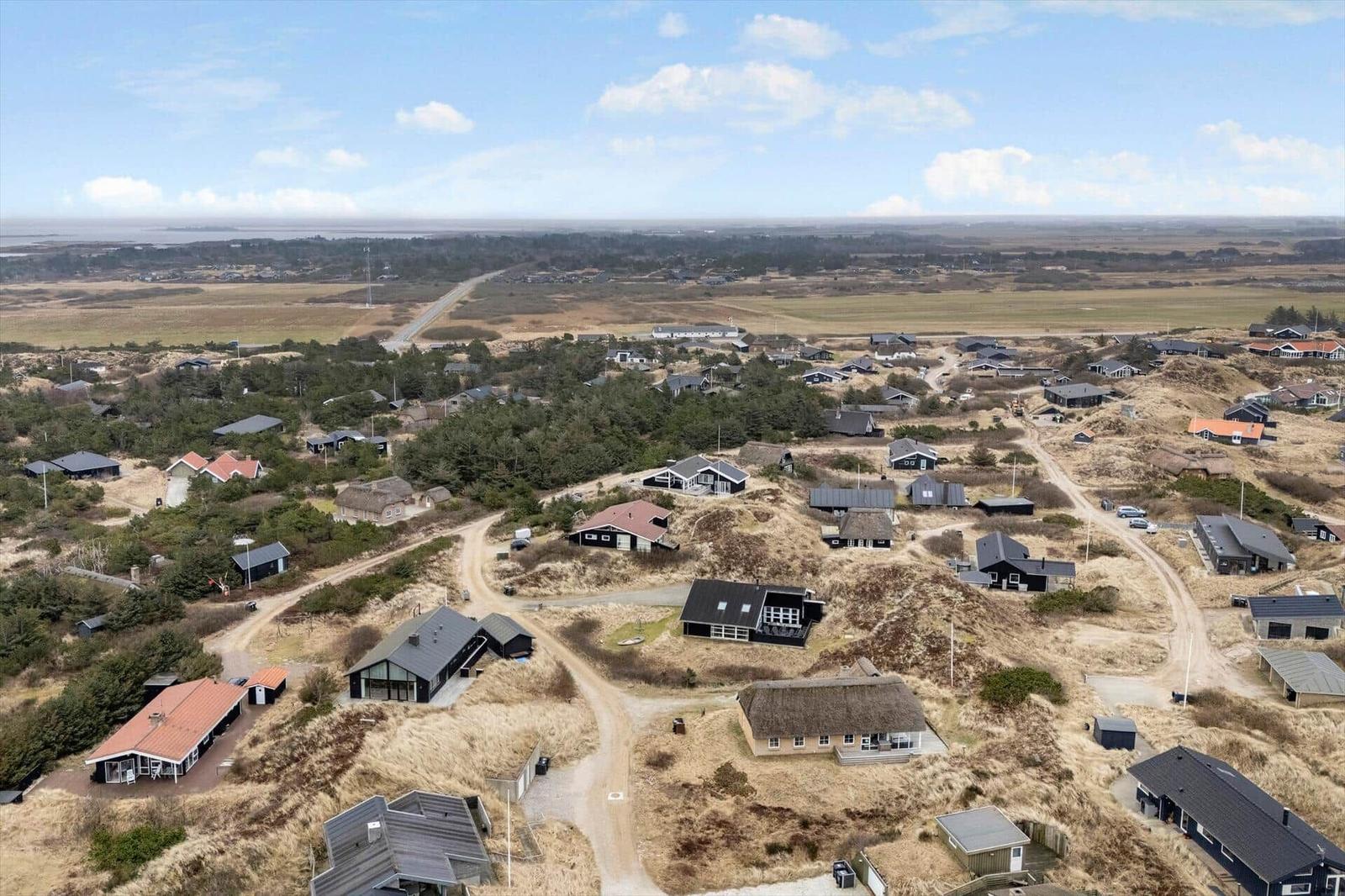 Aerial view of a coastal village with scattered houses and dunes.