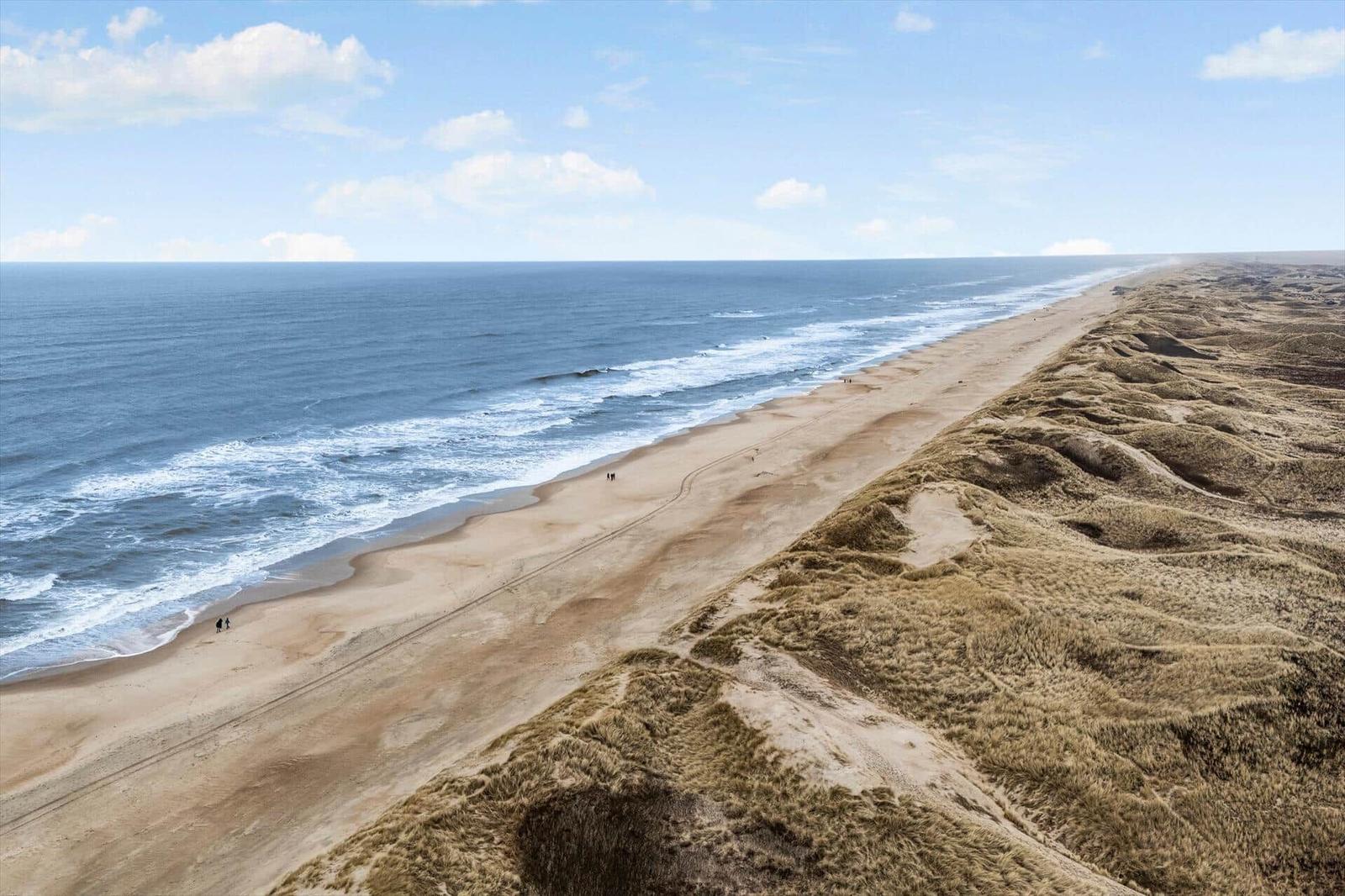 Strand mit Dünen und Meer unter blauem Himmel