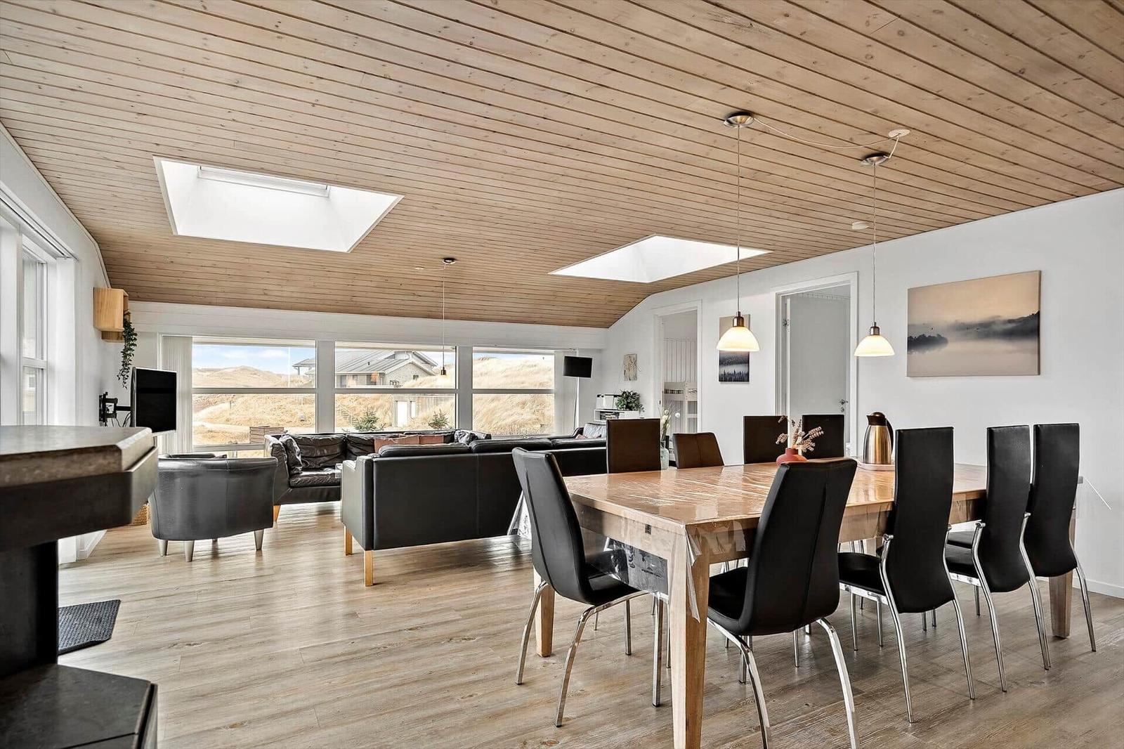 Großer Wohn- und Essbereich mit Holzboden, -decke und großen Fenstern.