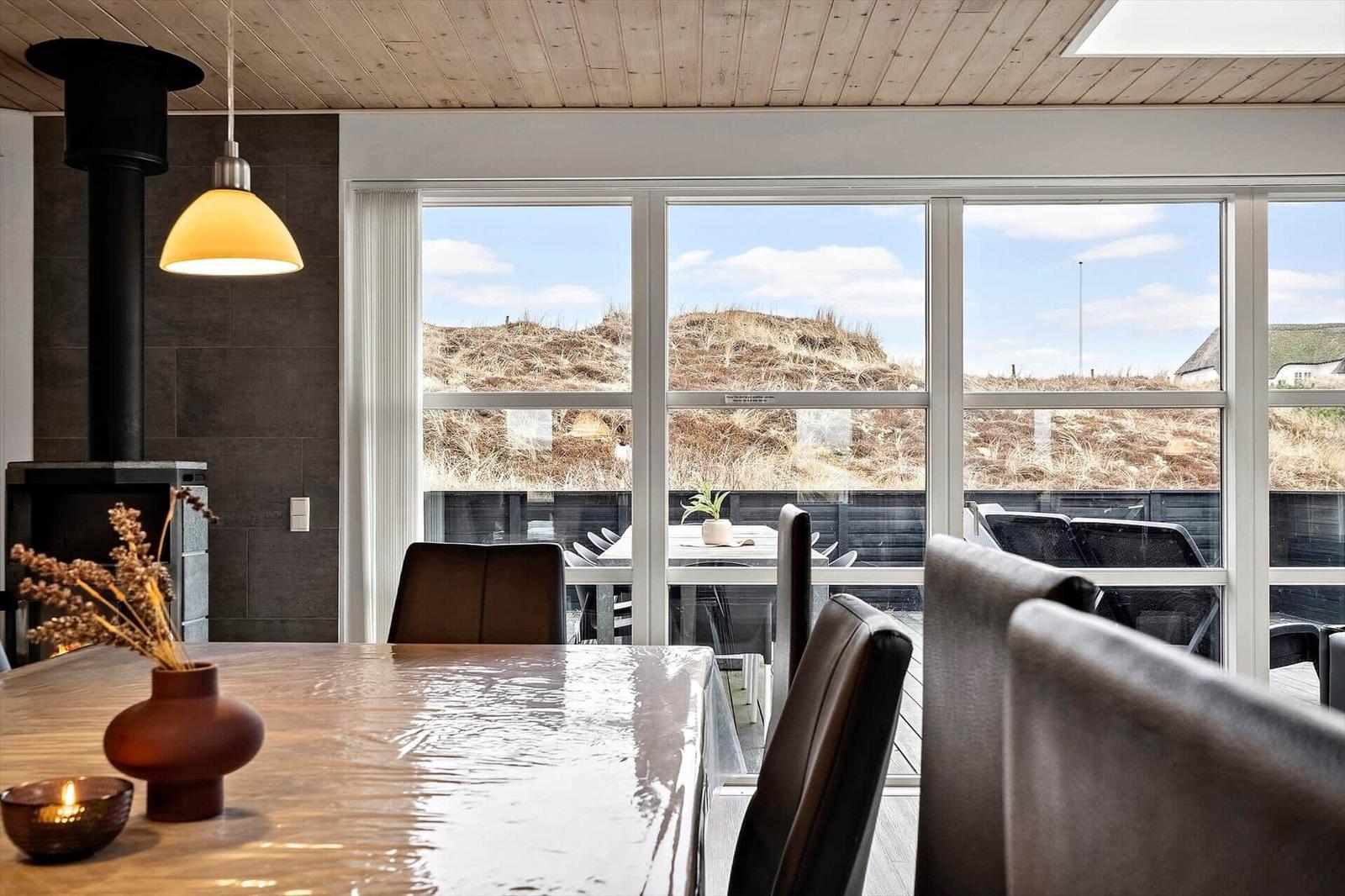 Esszimmer mit Holztisch, Stühlen und Blick auf Grashügel.