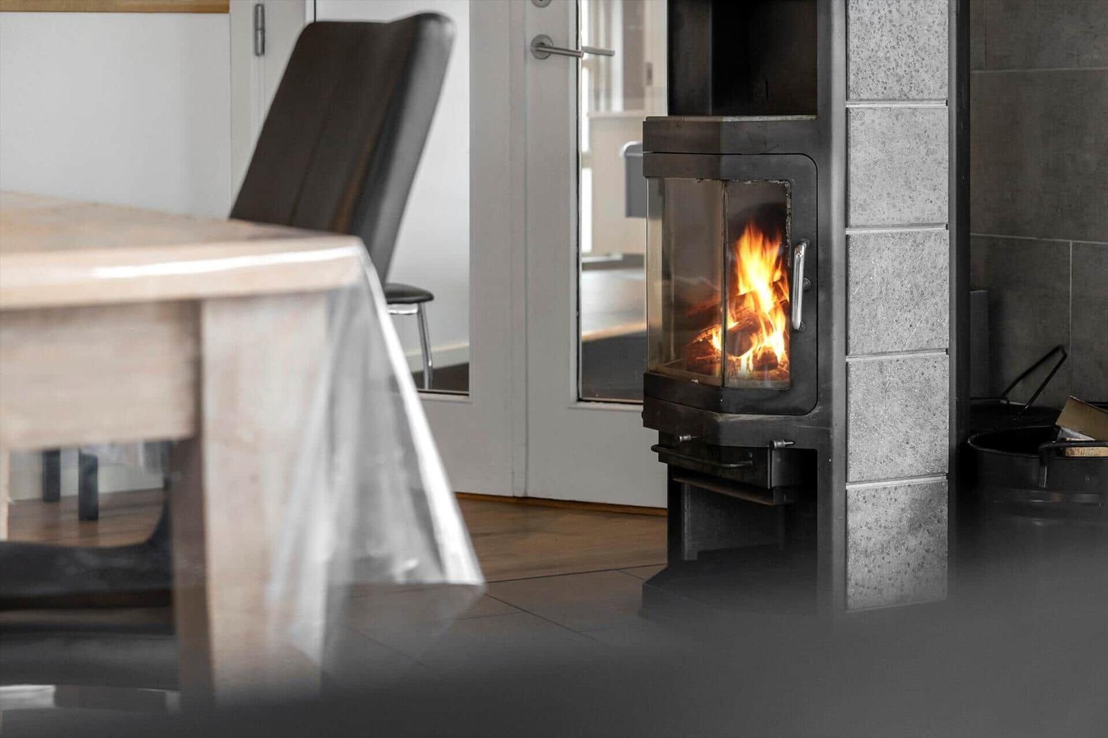 Ein Kamin mit brennendem Holz steht neben einem Tisch und Stuhl.