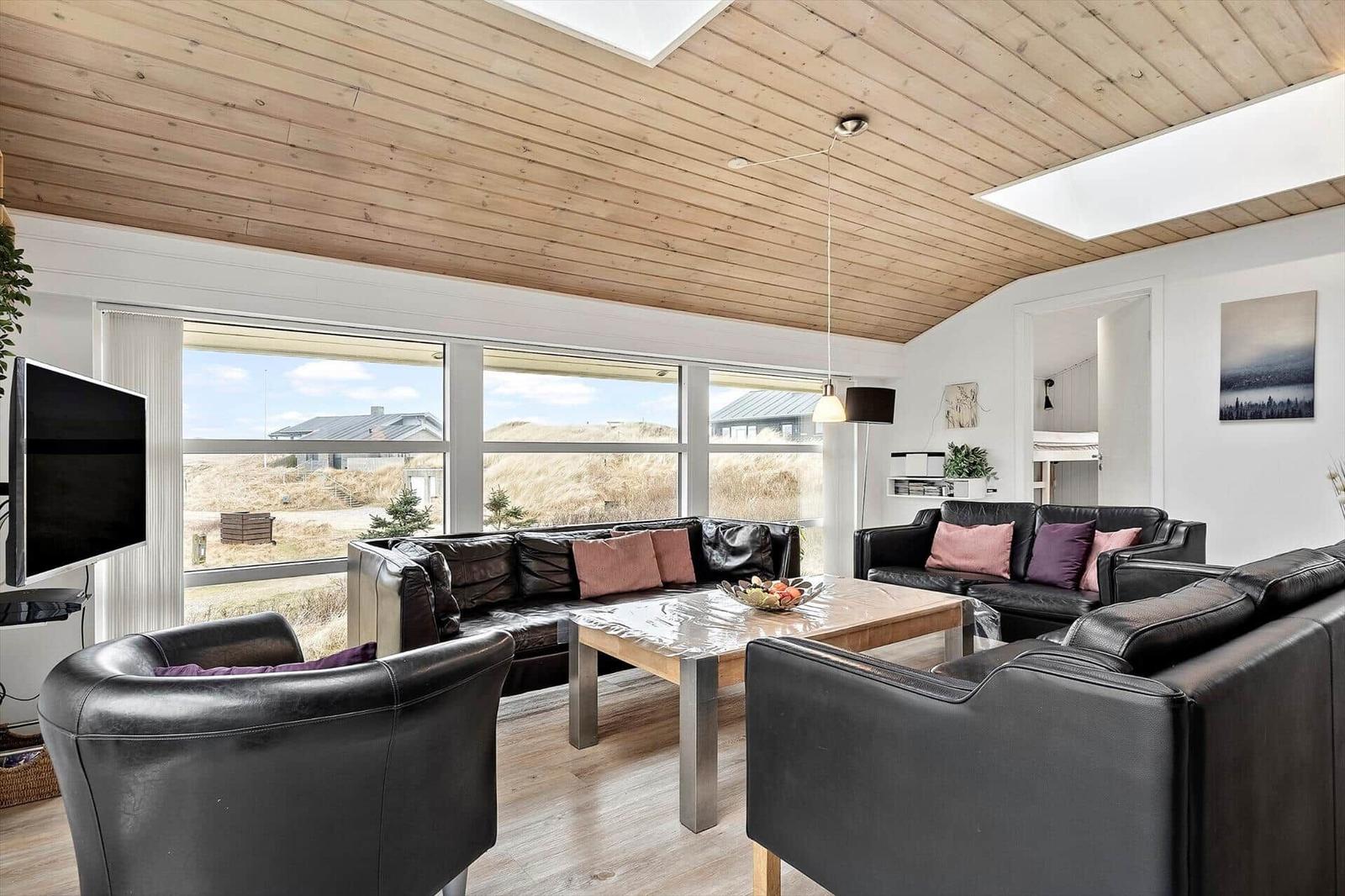 Wohnzimmer mit schwarzen Ledermöbeln, Holzdecke und großem Fensterblick