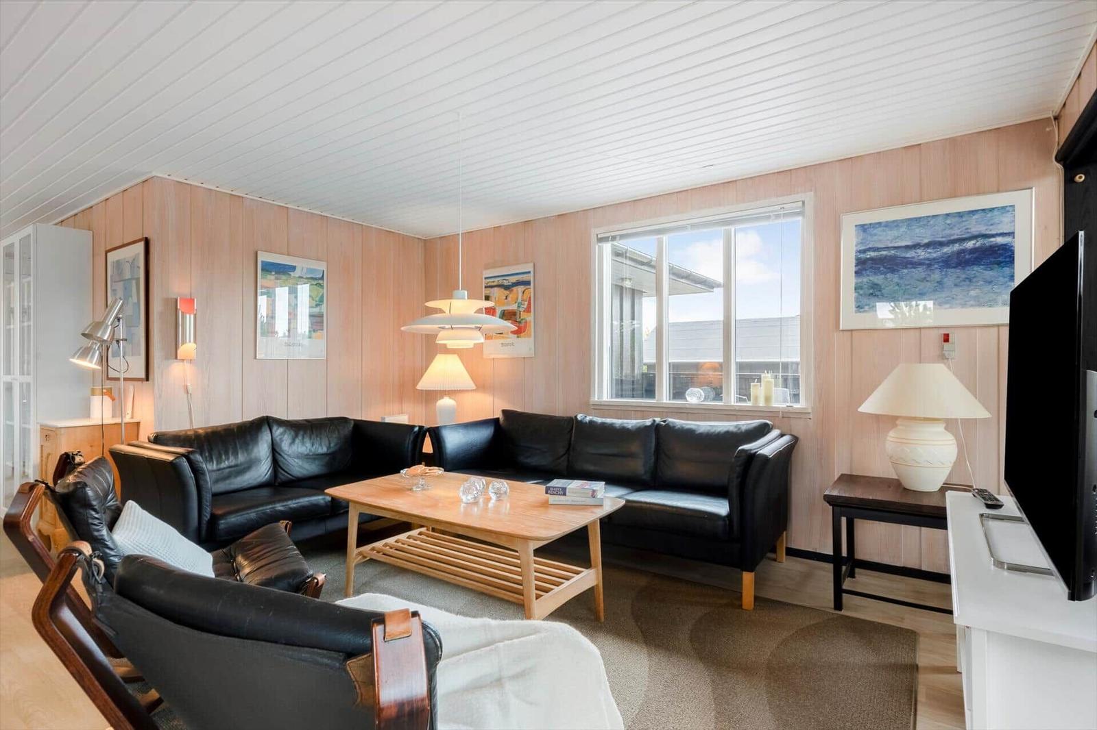 Wohnzimmer mit schwarzen Ledersofas, Holztisch und Fenster.