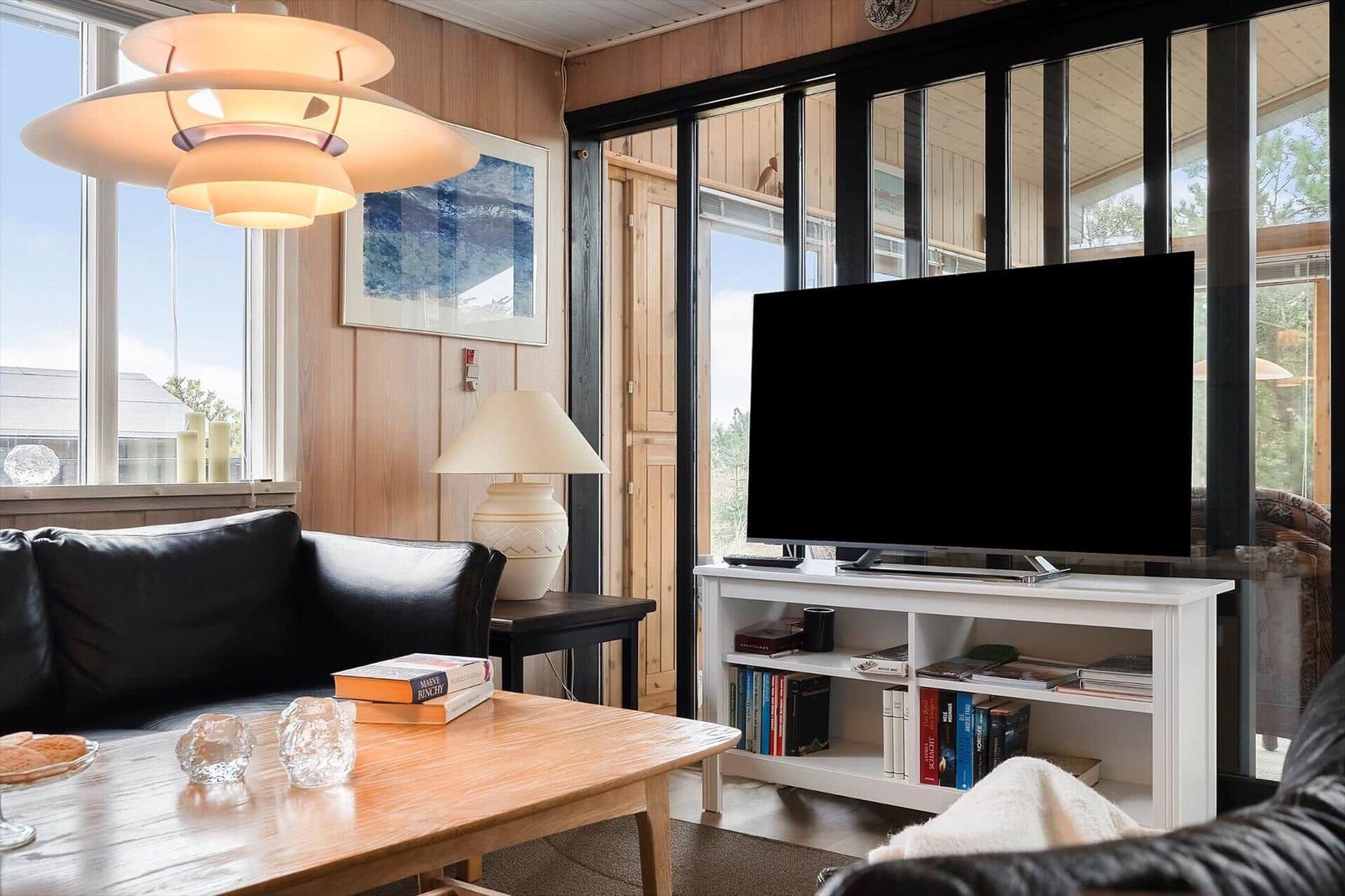 Wohnzimmer mit Sofa, Fernseher und Holztisch. Große Fenster und Holzwände.