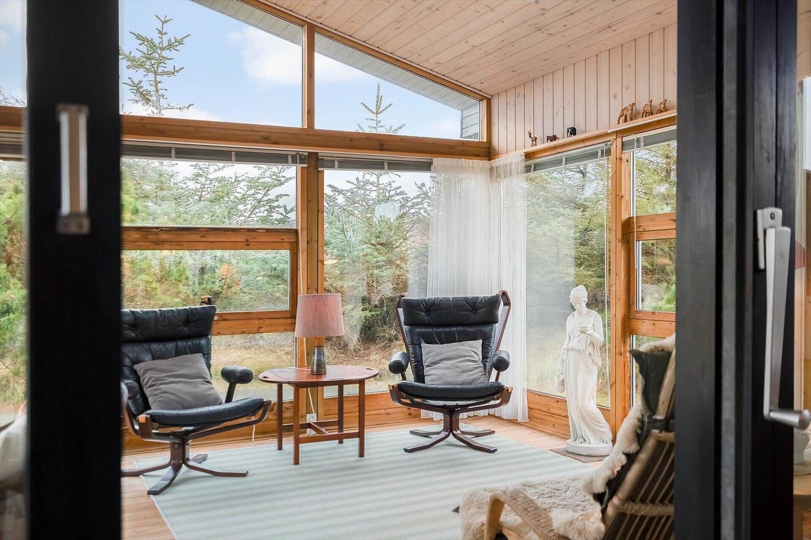 Zimmer mit zwei schwarzen Sesseln, Tisch und Blick auf Wald durch große Fenster.