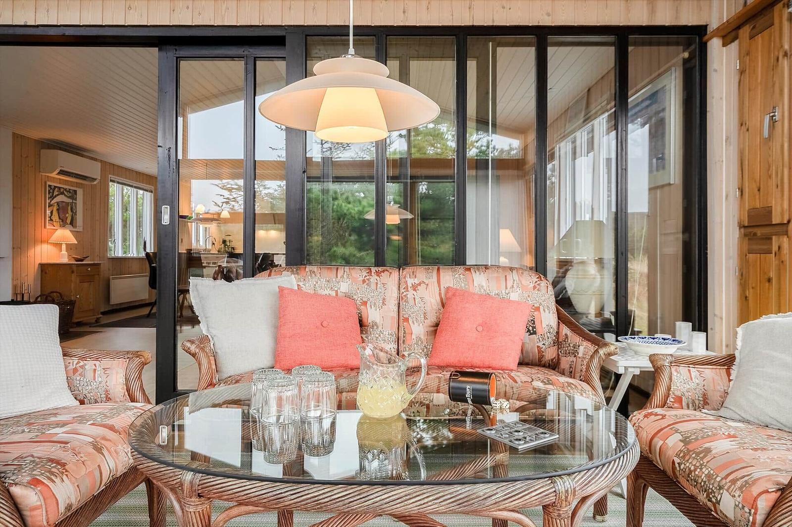Wohnbereich mit Sofa, Sesseln und Glas-Tisch. Große Fenster und Holzwände.