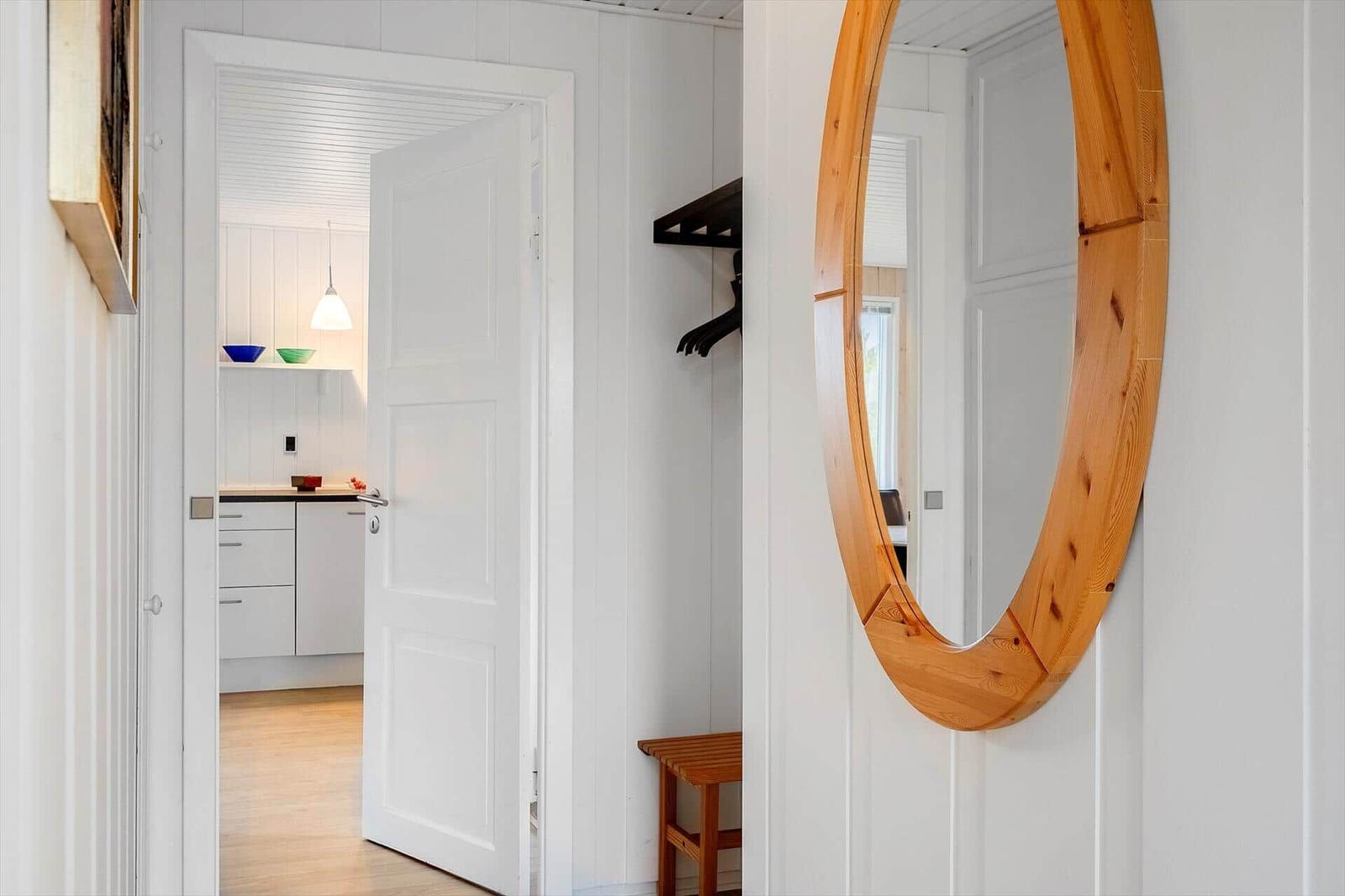 Hausgang mit runden Holzspiegel, Kleiderständer und Blick in die Küche.