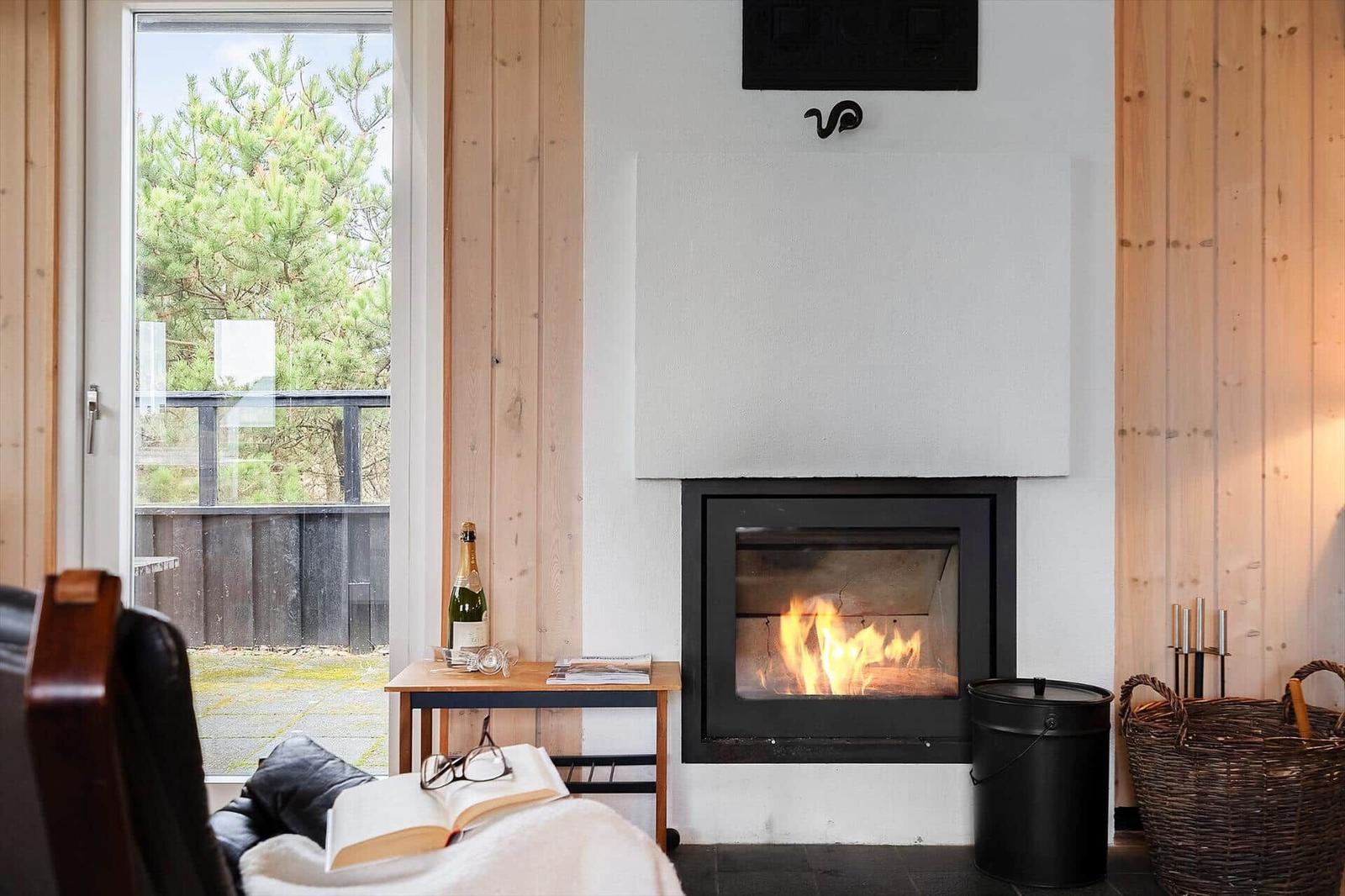 Kamin mit brennendem Feuer, Holzwände und Fensterblick auf Bäume.