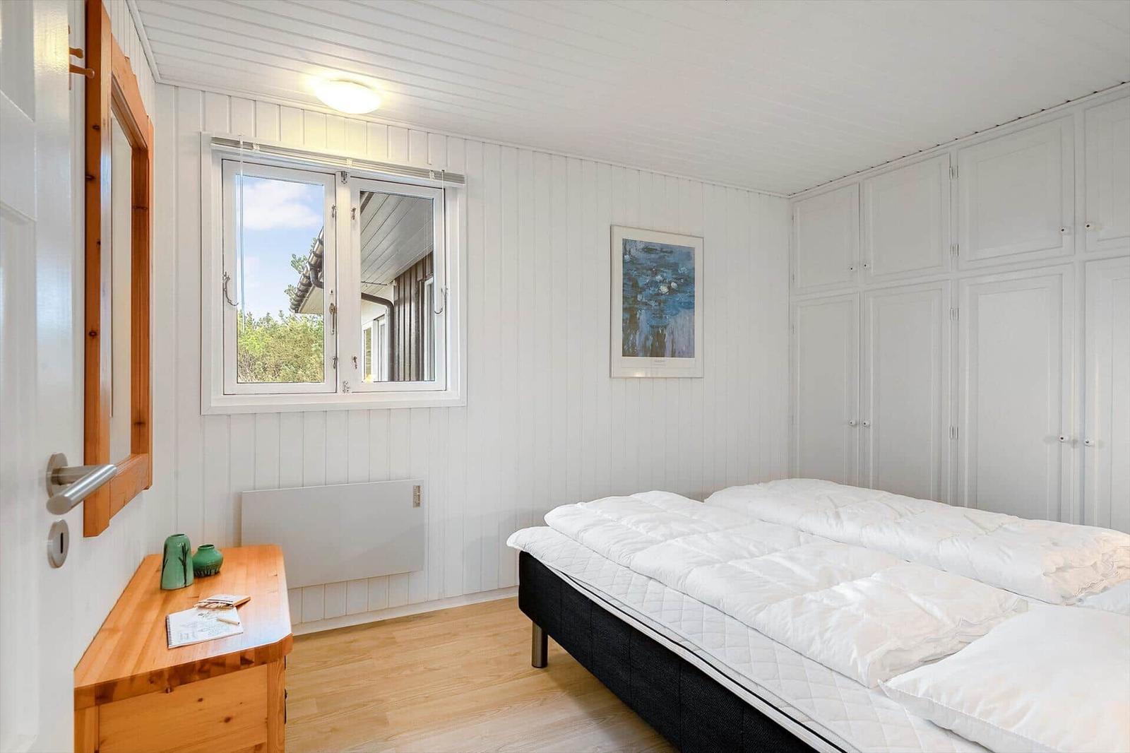 Schlafzimmer mit Doppelbett, weißer Einbauschränke und Holzoberfläche.