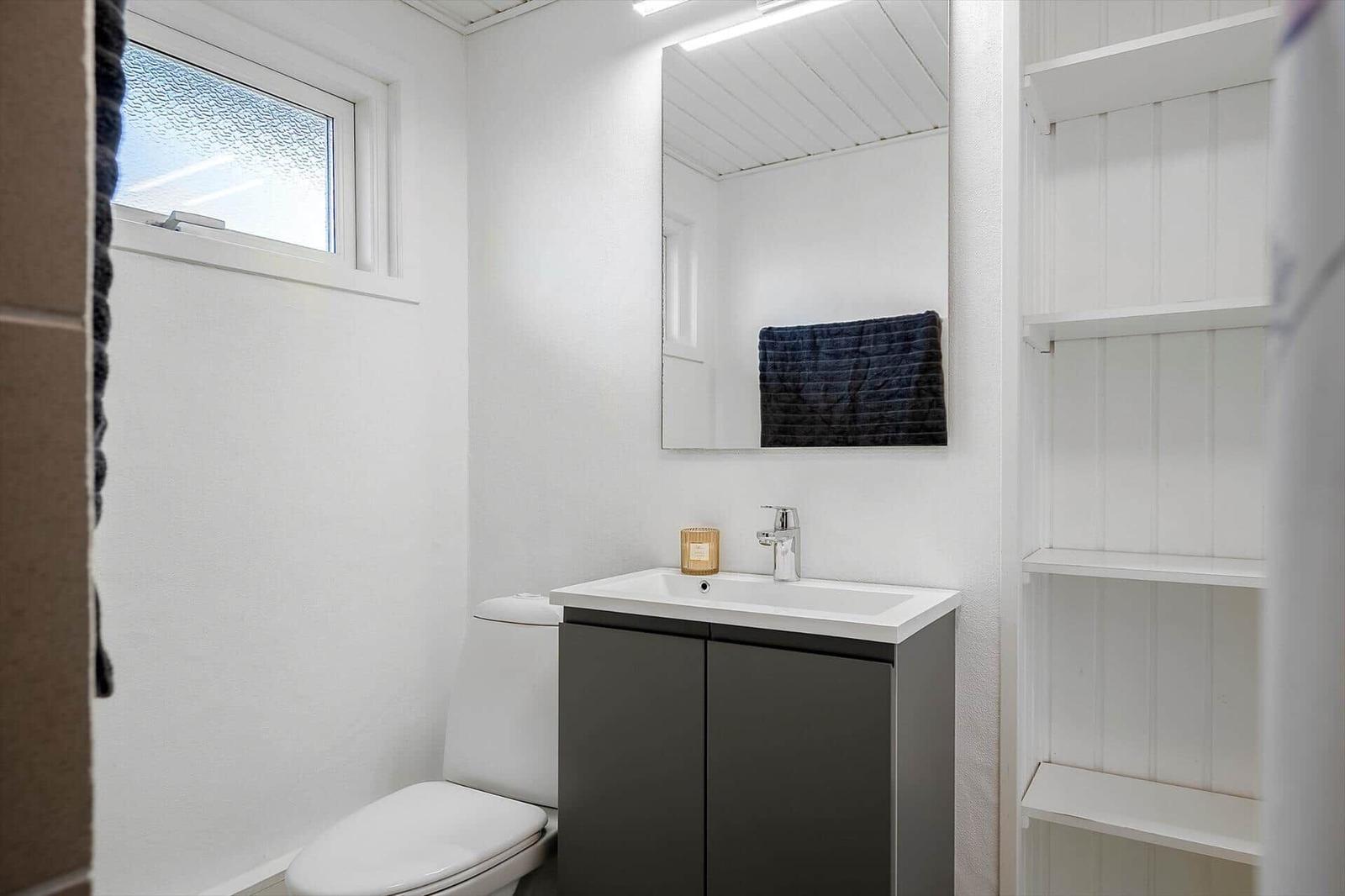 Badezimmer mit Toilette, Waschbecken und Spiegel. Fenster und Regal sichtbar.