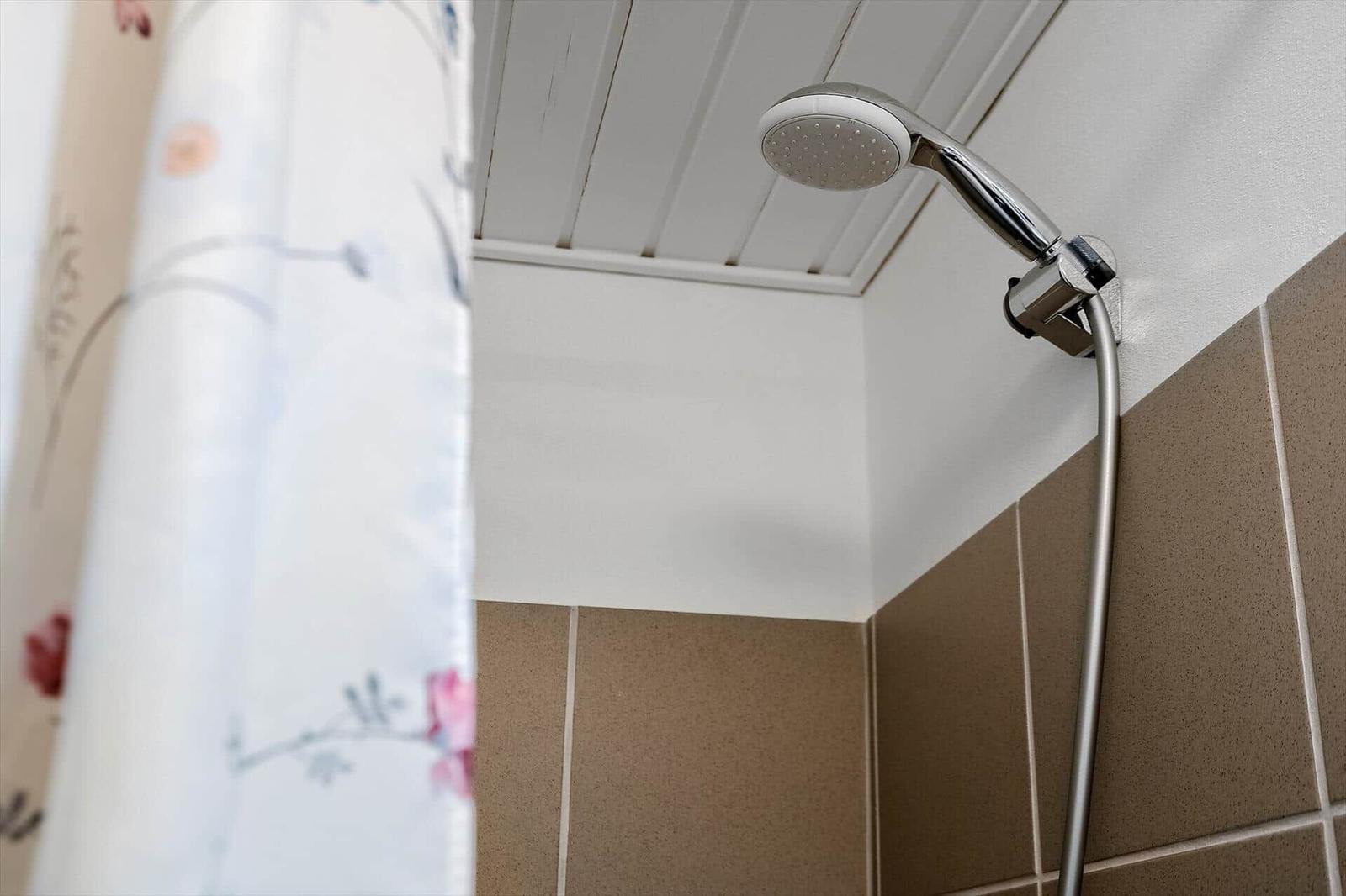Duschkopf an der Wand, braune Fliesen und weiße Decke mit Holzverkleidung.