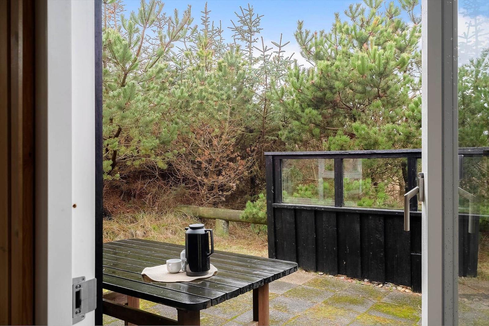 Terrasse mit Tisch und Kanne, Blick auf Nadelbäume