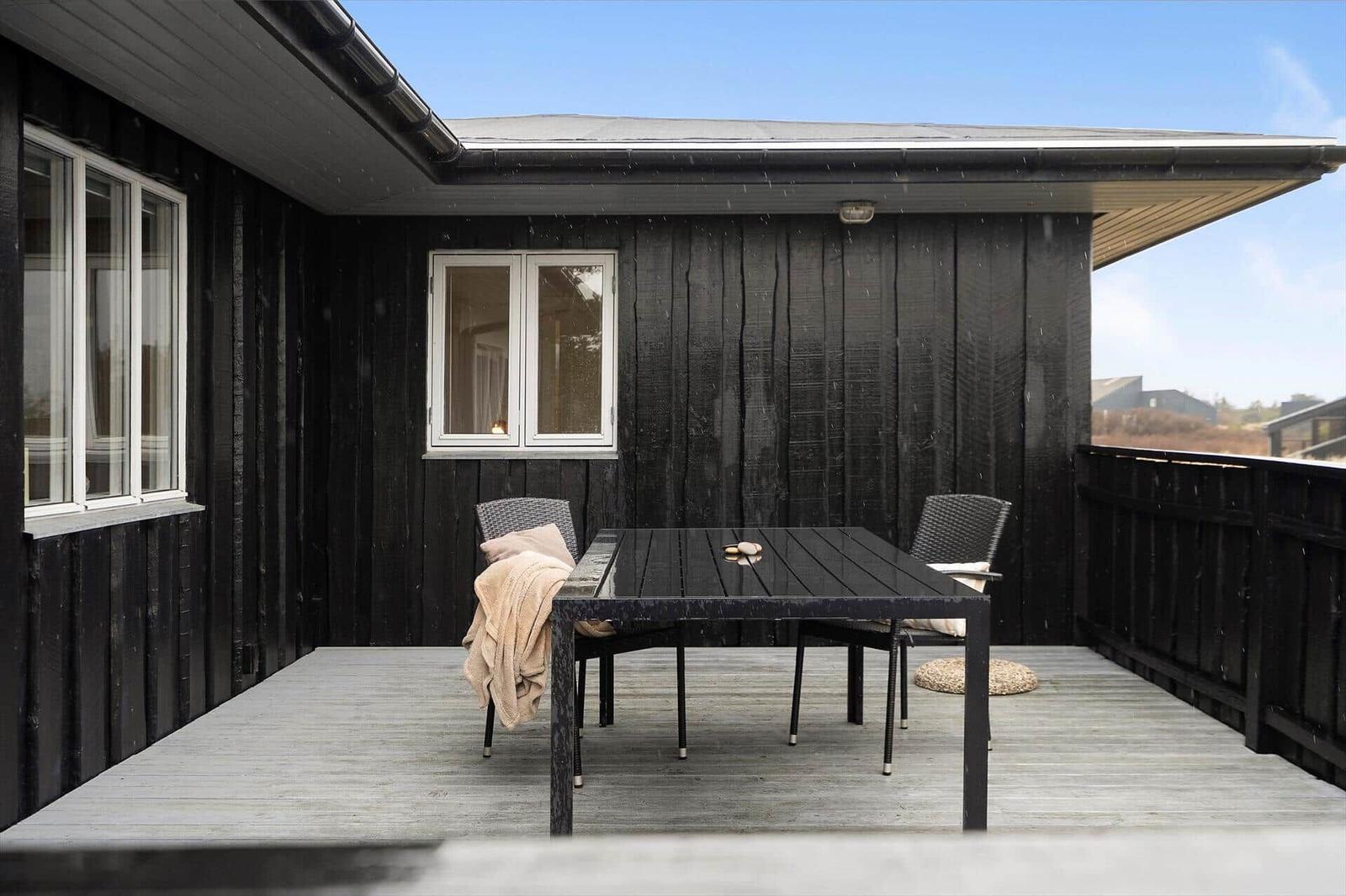 Terrasse mit Tisch und Stühlen vor schwarzem Holzhaus