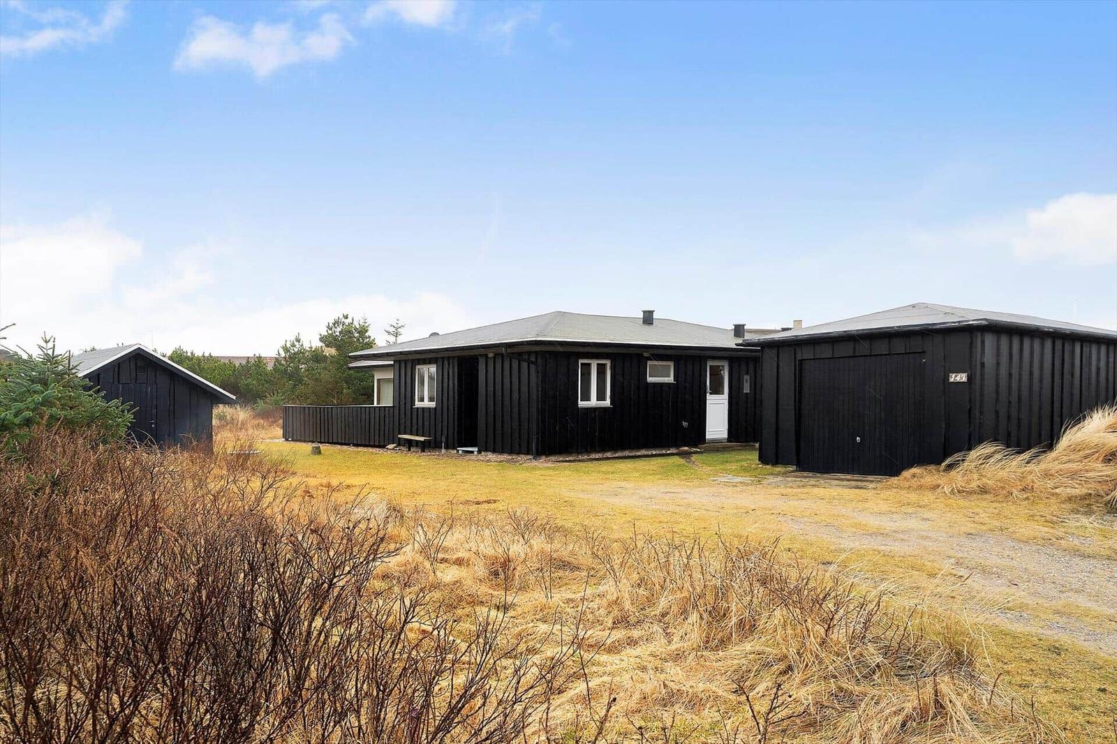 Schwarzes Holzhaus mit Garage und kleinem Nebengebäude auf grünem Grundstück.