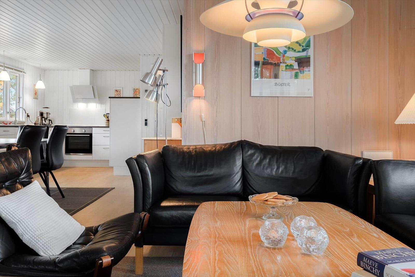 Wohnzimmer mit Ledersofa, Holztisch und Küchenbereich im Hintergrund.