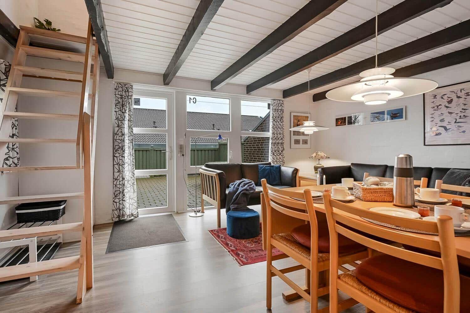 Wohn- und Essbereich mit Holztreppe, Sofa, Esstisch und Fenster zur Außentür.