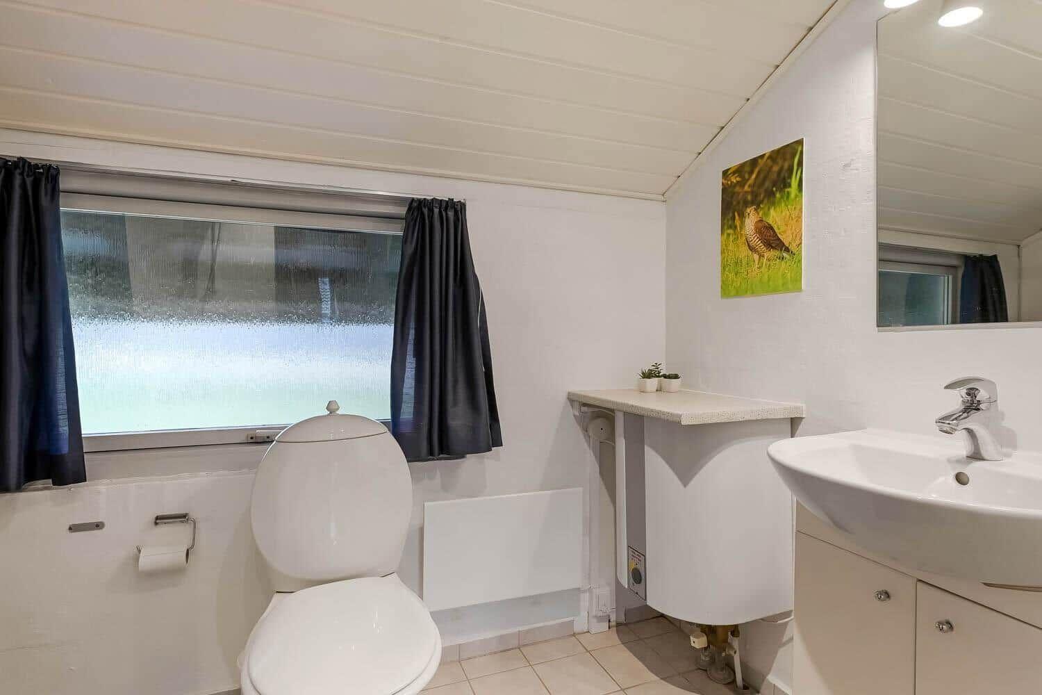 Badezimmer mit Toilette, Waschbecken und Fenster mit Vorhängen.