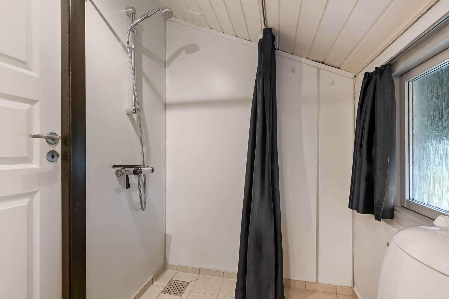 Dusche mit Duschbrause, schwarzer Vorhang und Fenster mit Milchglas.