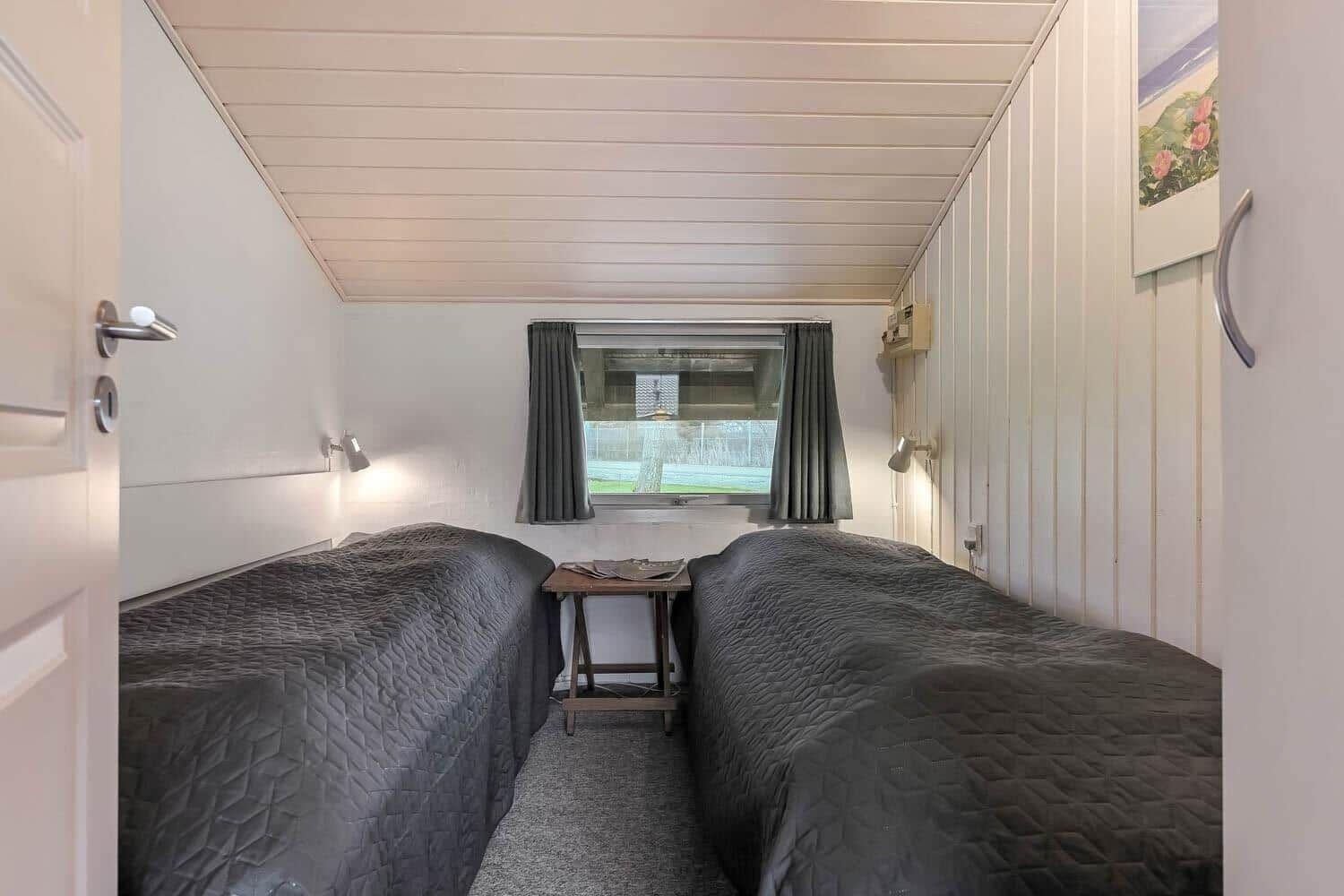 Zwei Betten mit dunklen Bettdecken stehen gegenüber einem Fenster mit grauen Vorhängen.