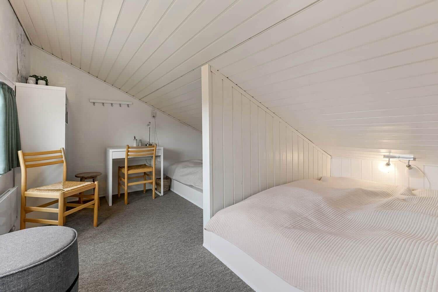 Schlafzimmer mit Doppelbett, kleinem Schreibtisch und Stuhl unter schrägem Dach.