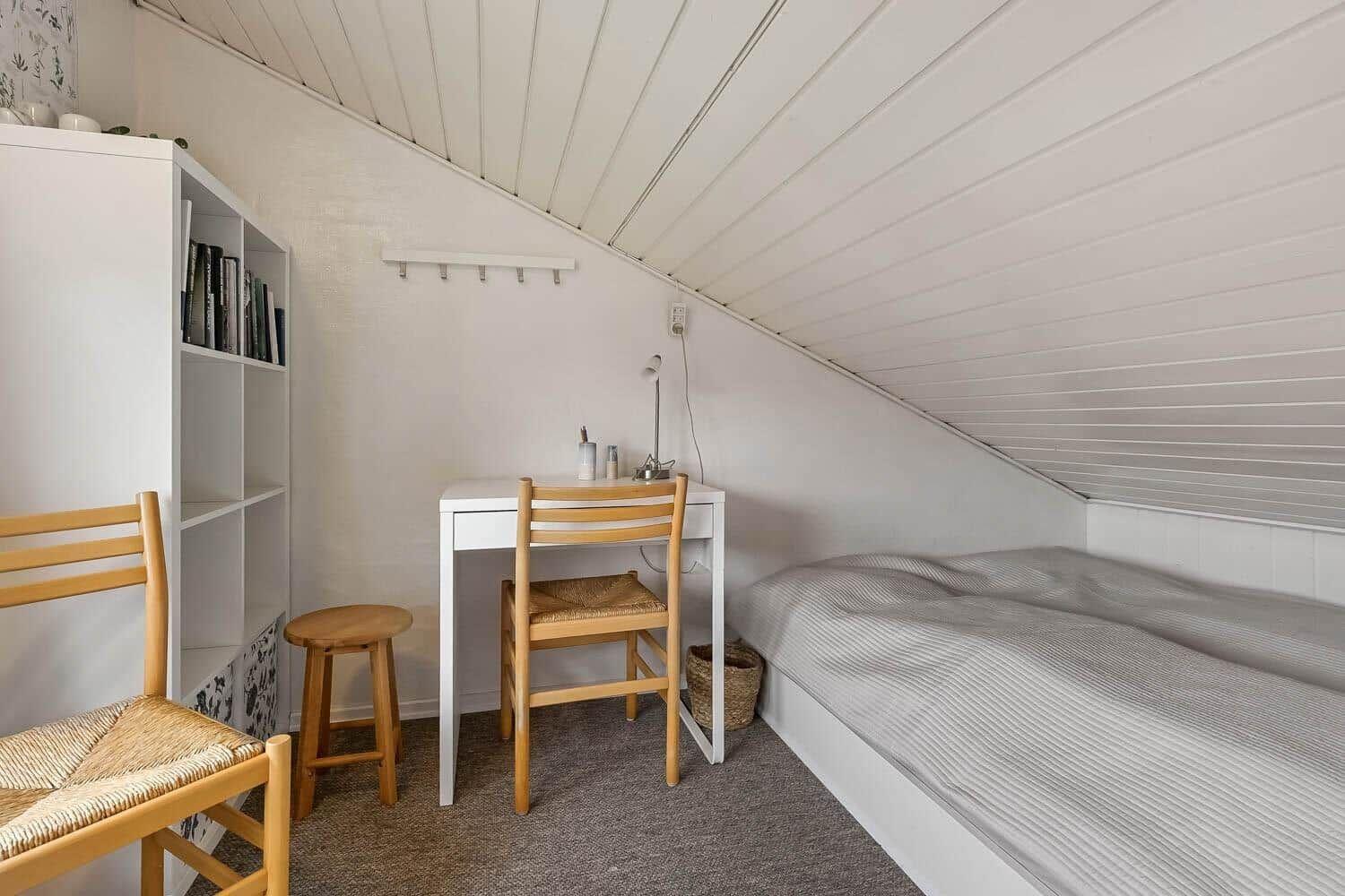 Ein Schlafzimmer mit Dachschräge, Bett, Schreibtisch und Stuhl.