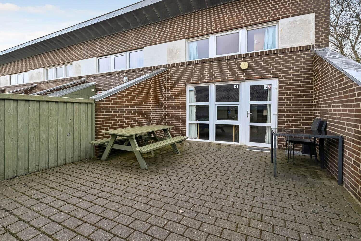Terrasse mit Picknicktisch, Tisch und Stühlen vor einer Wohnung mit Glasfront.