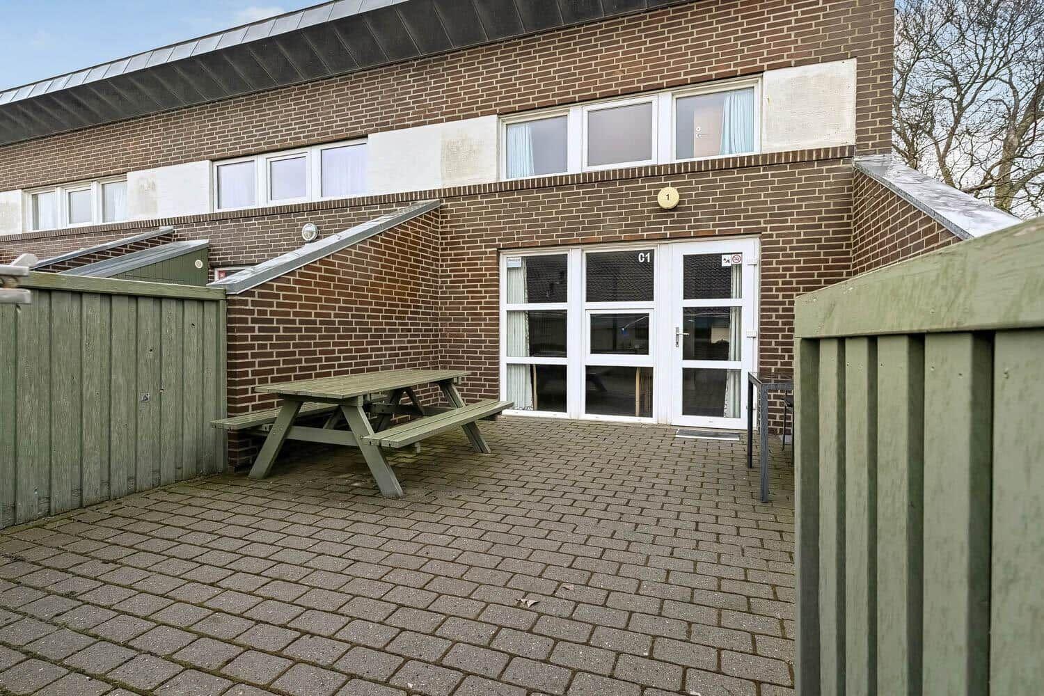 Haus mit Terrasse, Tisch und Gartenzaun. Eingangstür mit Nummer C1.