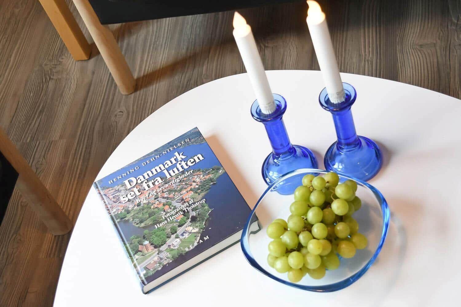 Runde Tisch mit Buch, zwei Kerzenhaltern und einer Schale Trauben.