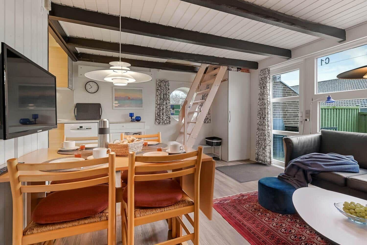 Essbereich mit Tisch, Stühlen und Fernseher. Wohnbereich mit Sofa und Kissen. Treppenhaus zur oberen Etage.