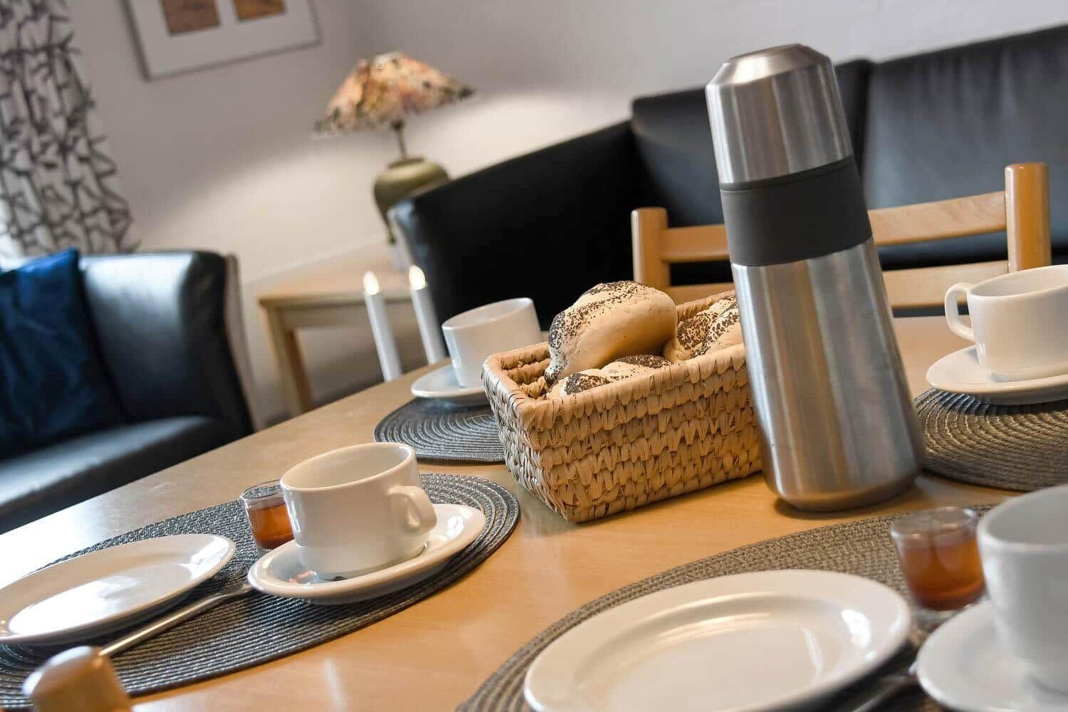 Tisch mit Tassen, Tellern, Brotkorb und Thermoflasche