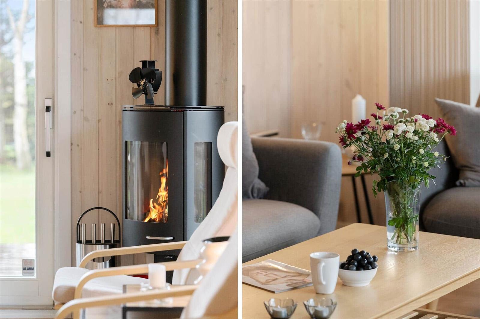 Wood-burning stove, gray sofa, table with flowers and fruit.
