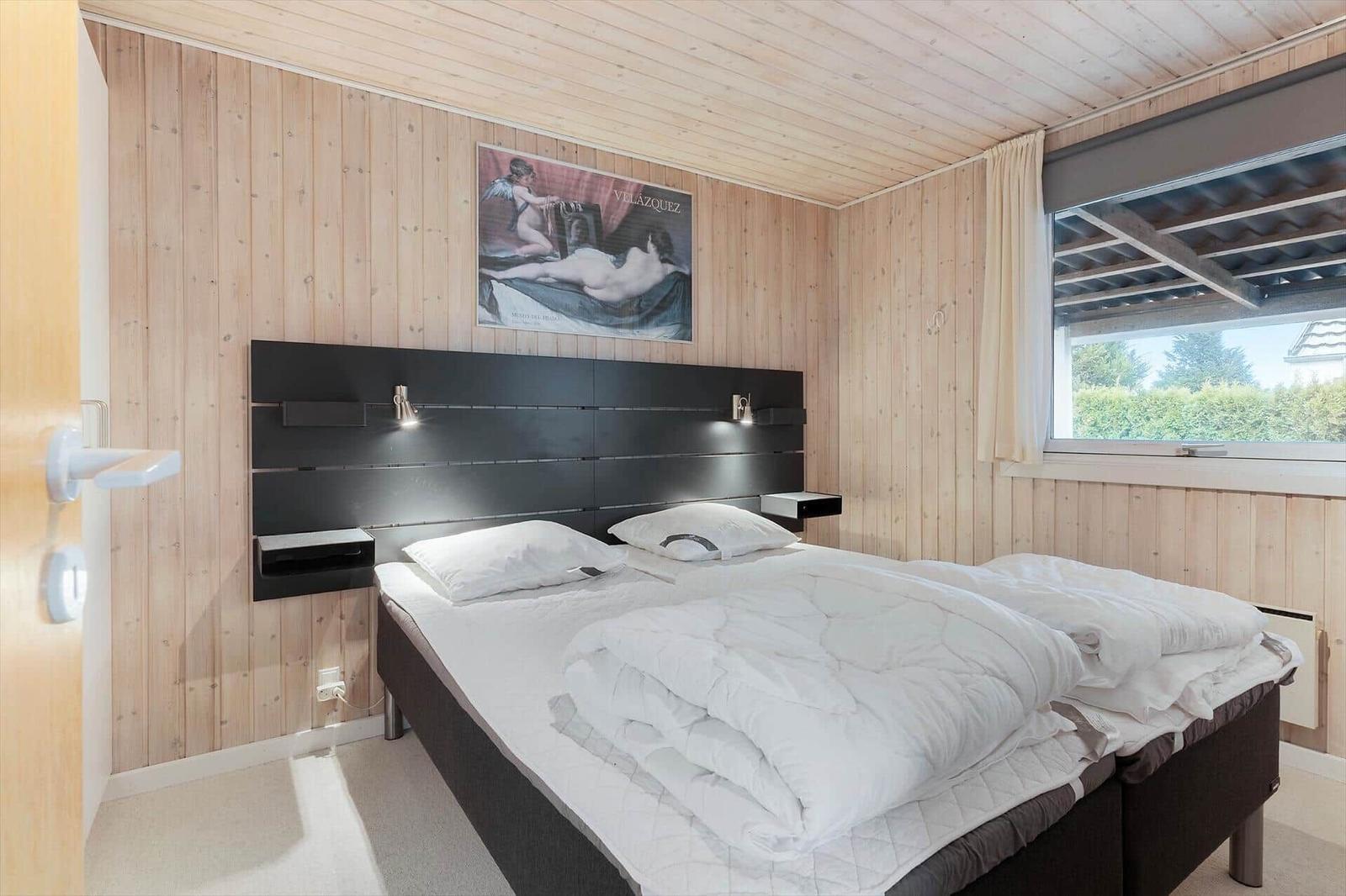 Bedroom with wooden walls, bed, and window overlooking greenery.
