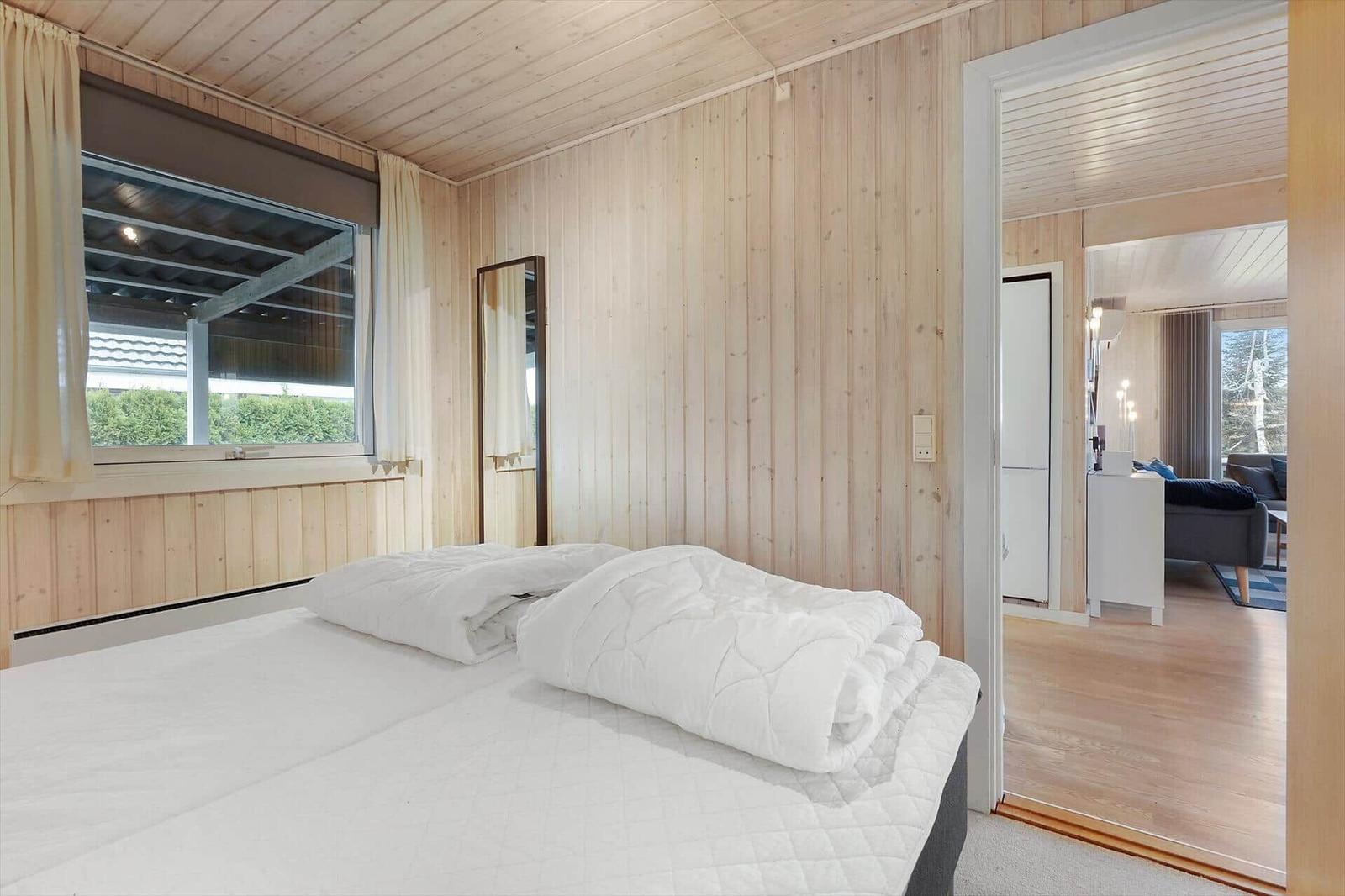 Bedroom with bed, wooden walls, and view into the living room.