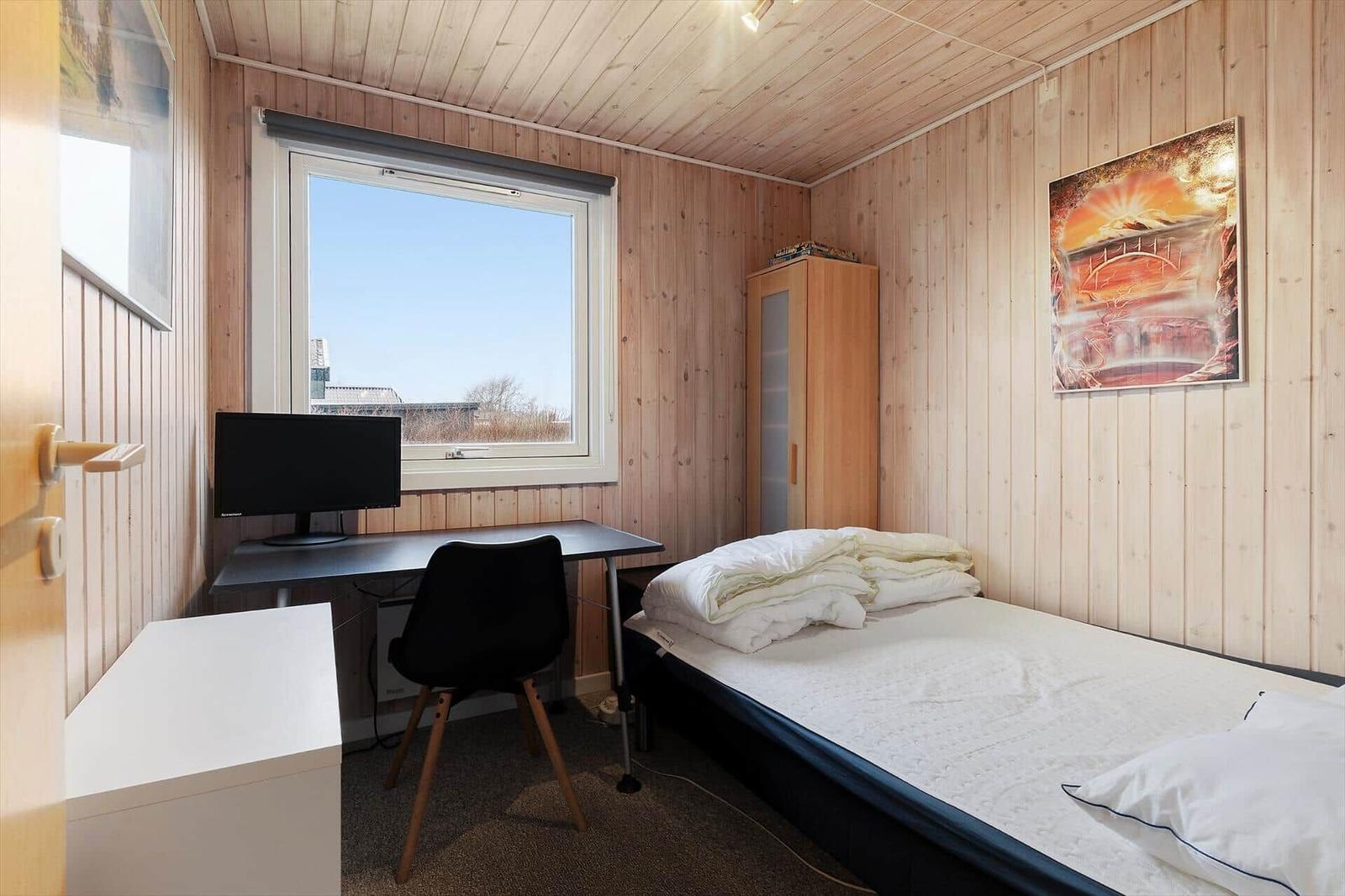 Bedroom with bed, desk, and window. Wooden walls and wall art.