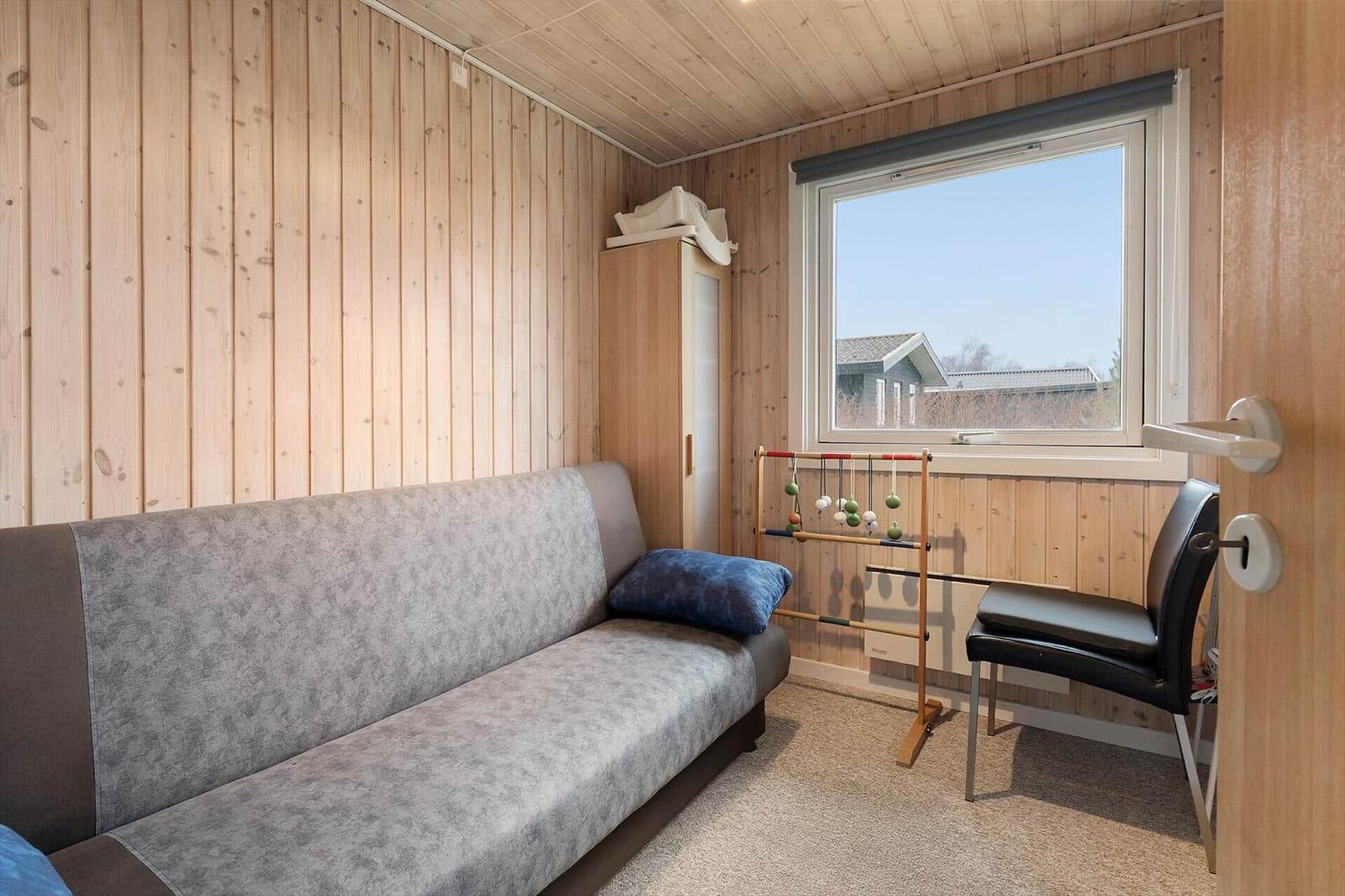 A room with sofa, chair, and wardrobe. Wooden walls and a window with view outside.