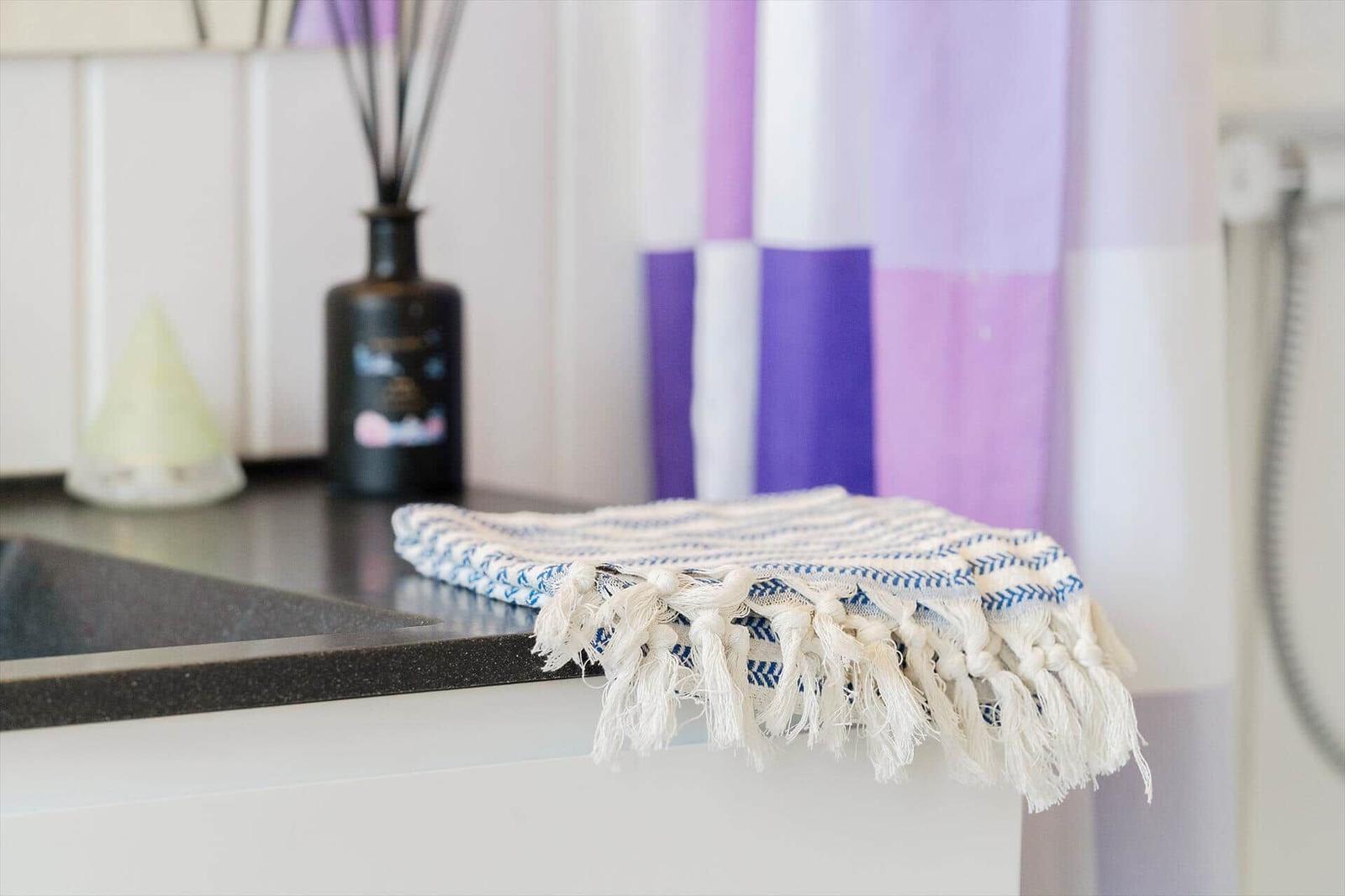 A towel rests on the countertop in front of a shower curtain with purple and white stripes.