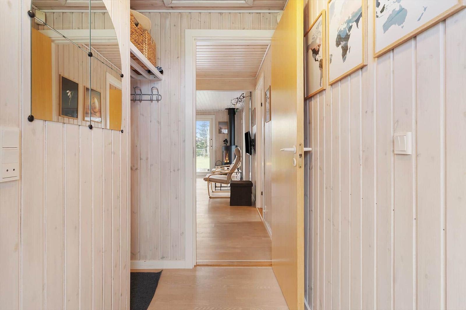 Hallway with wooden walls and view into living area with fireplace and chair.