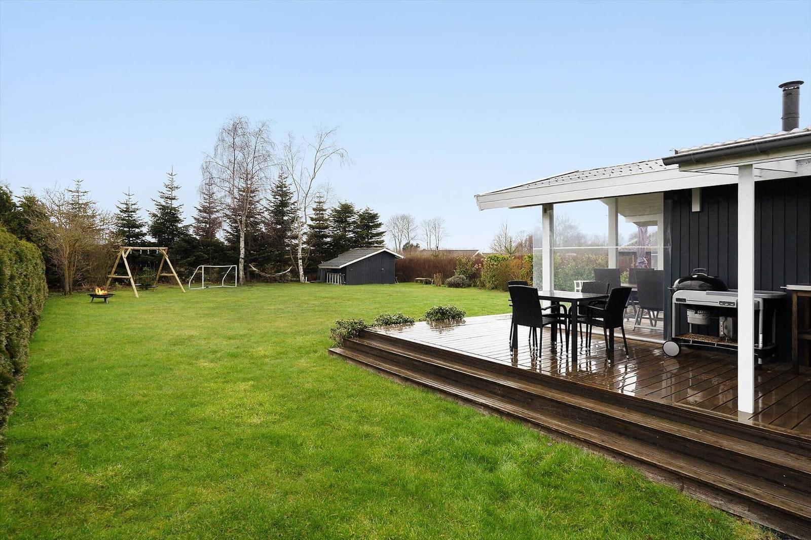 Deck with grill and table. Lawn with playground and shed.