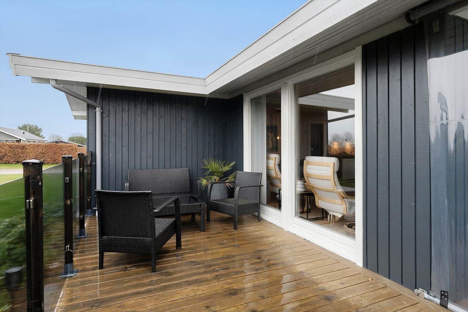 Deck with dark outdoor furniture and glass railing. View into the interior of the house.