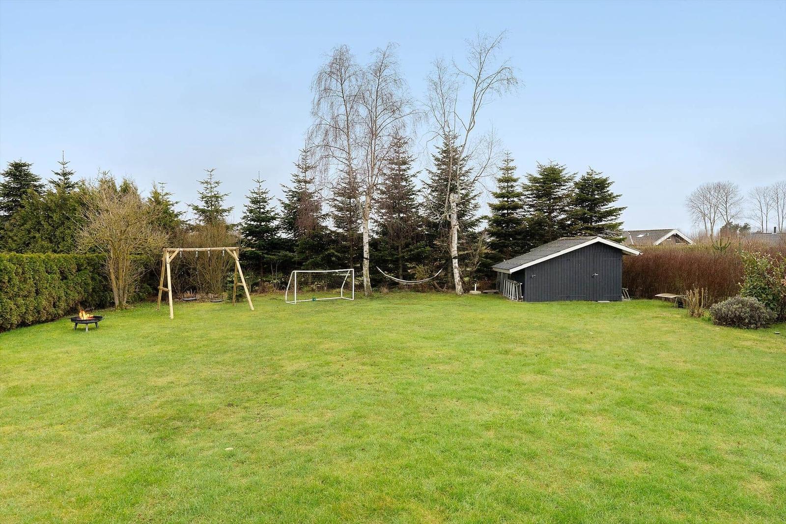 Green lawn with fire pit, swing, soccer goal, and shed.