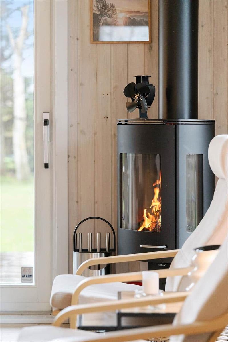 A fireplace with burning fire stands next to a window and a chair.