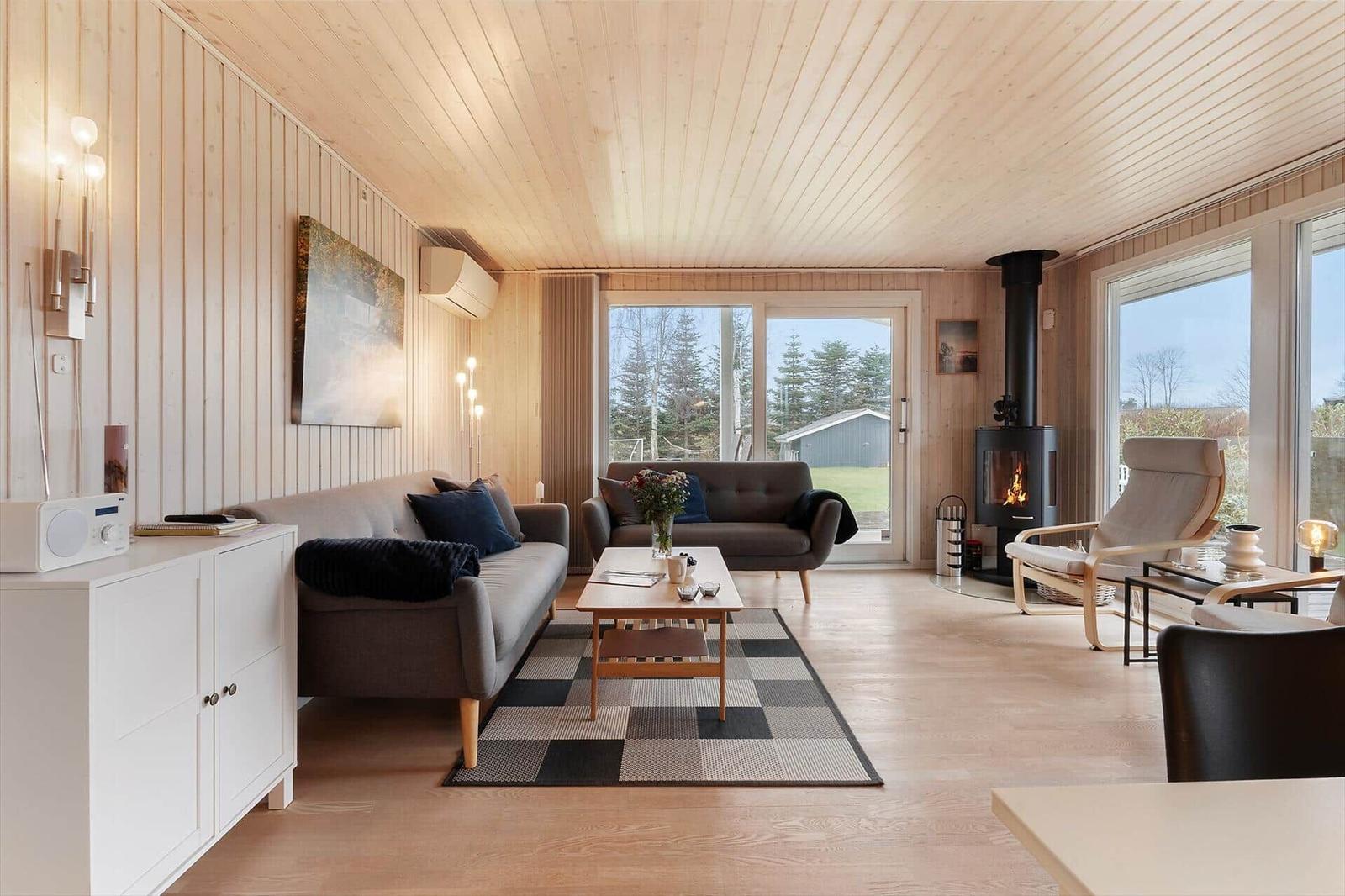 Living room with wood walls, sofa, fireplace, and large windows.