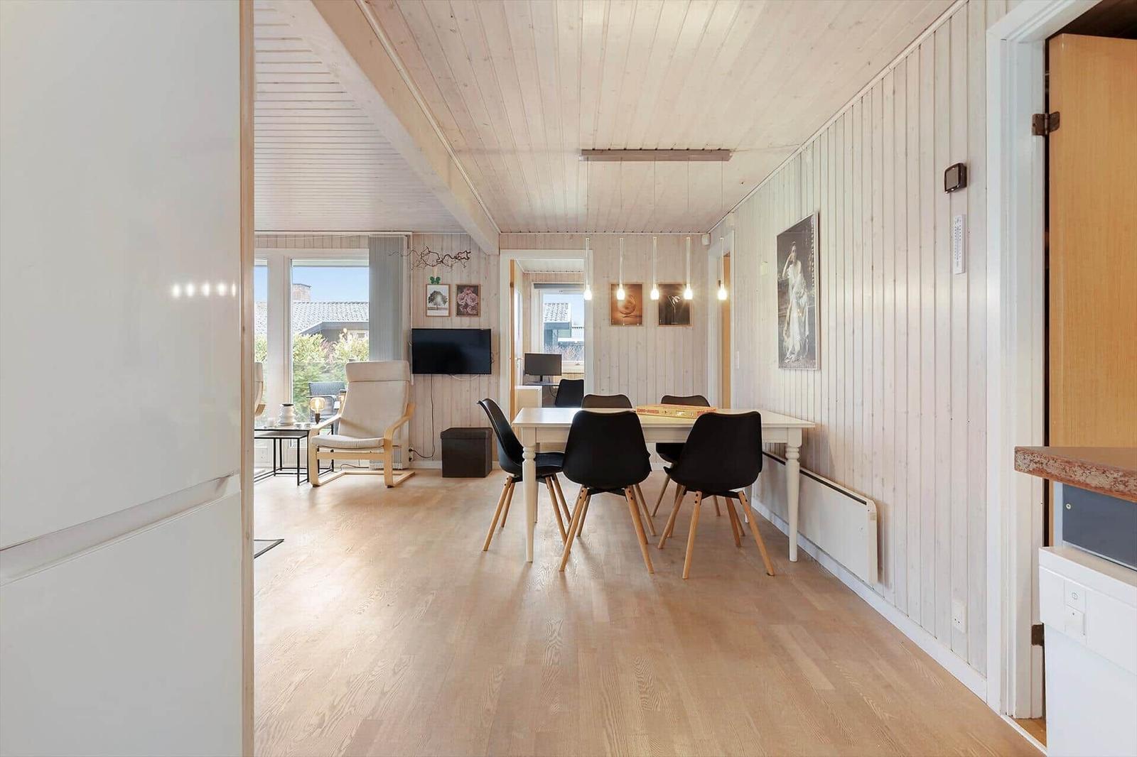 Dining area with table and chairs, living area with armchair and TV, wooden floor and white walls.