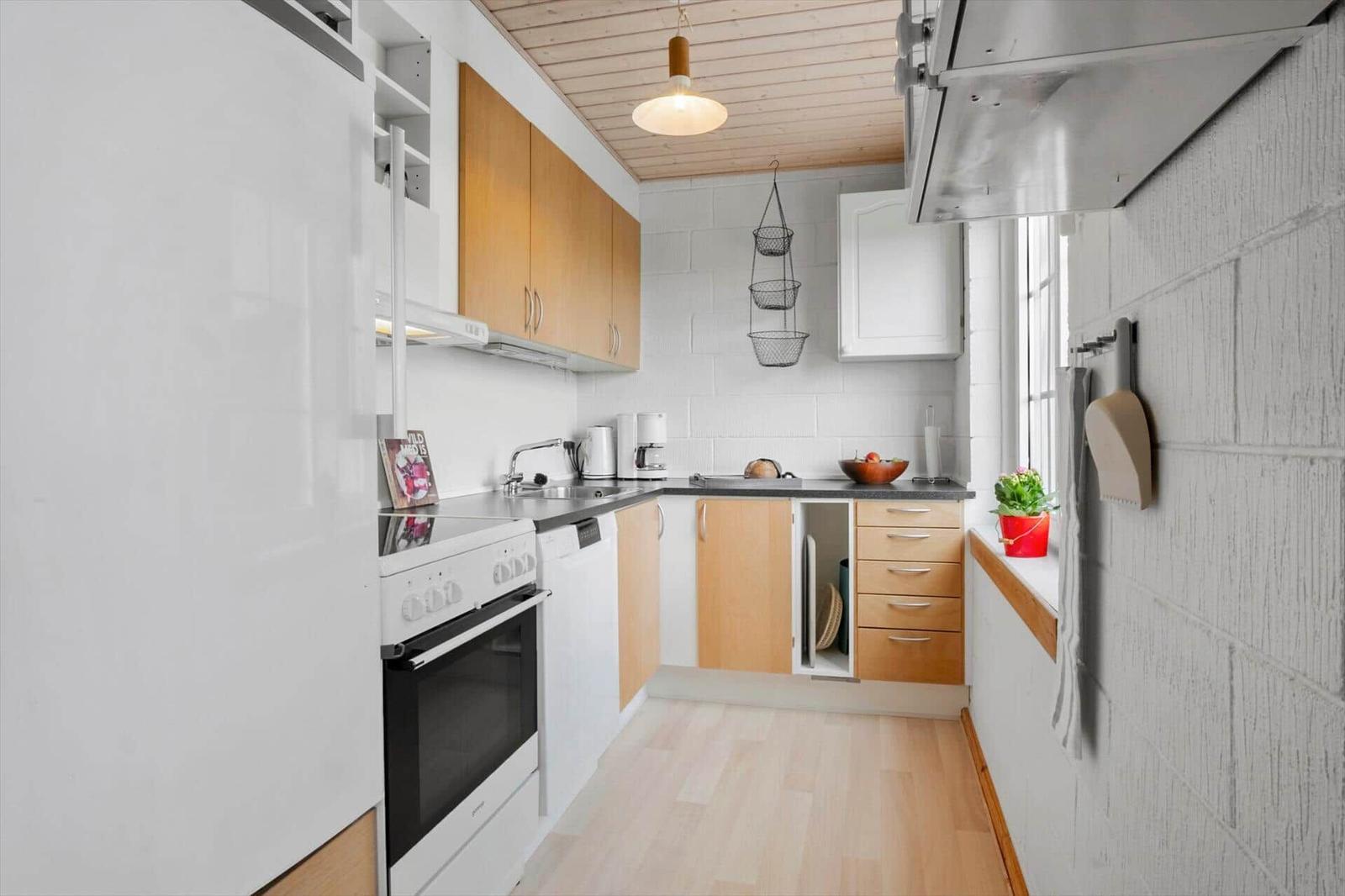 Küche mit Holzoberflächen, weißen Schränken und Fensterbank mit Pflanze.